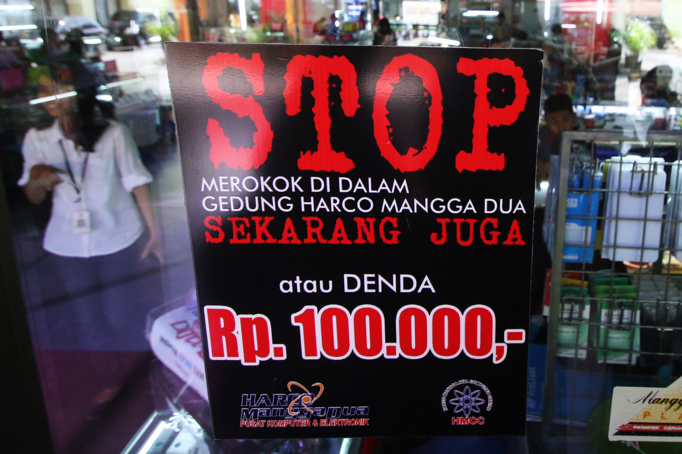 Sebuah poster peringatan bagi perokok dikenai denda Rp100 ribu. Meroko juga bisa memicu covid-19 karena menurunnya imunitas. 