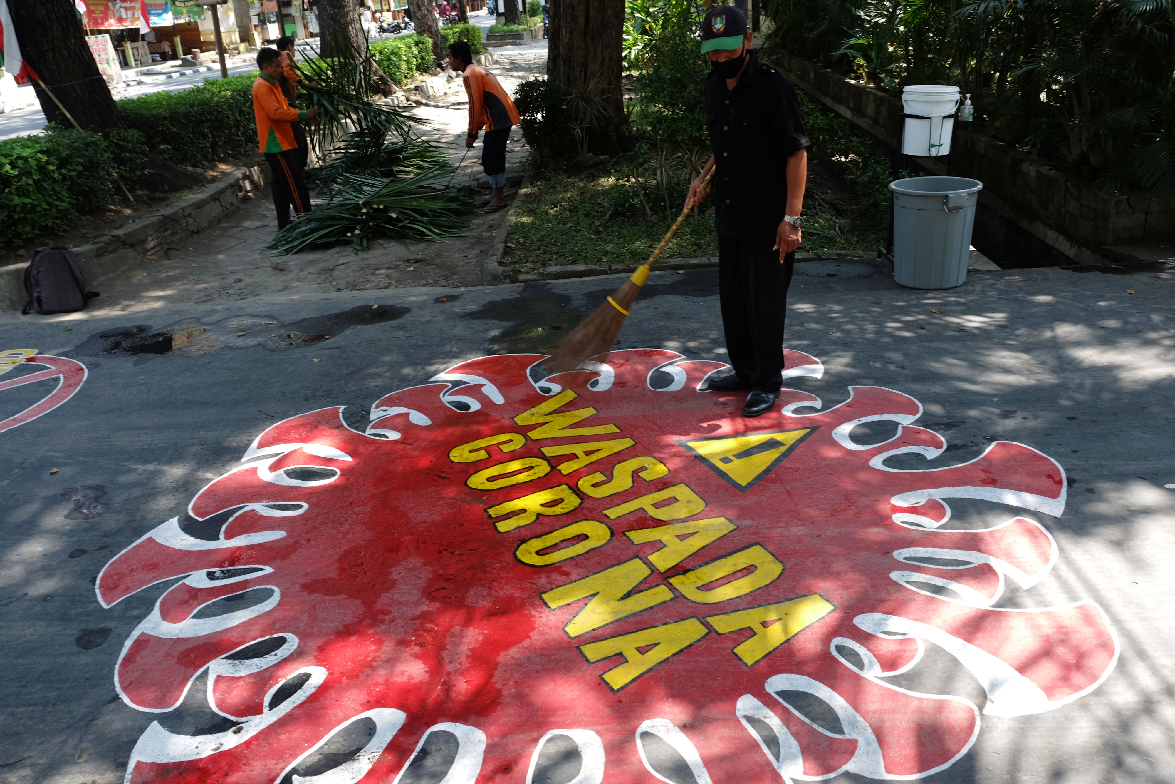 Pekerja membersihkan jalan yang terdapat mural berisi pesan Waspada Penyebaran Virus Korona di halaman Kantor Dinas Lingkungan Hidup, Solo. 