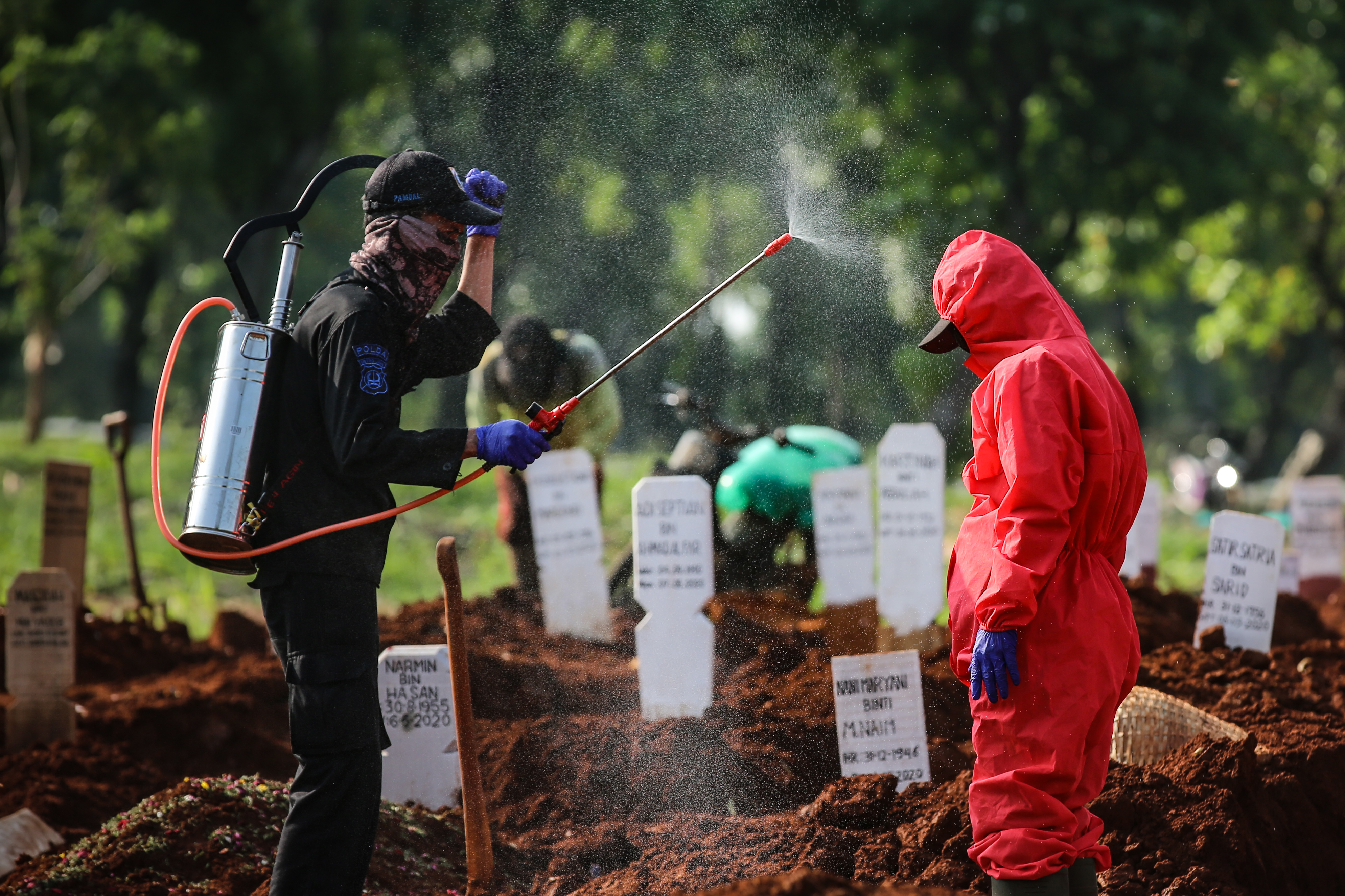 Petugas menyemprotkan cairan disinfektan kepada petugas yang baru selesai menguburkan pasien positif covid-19. 