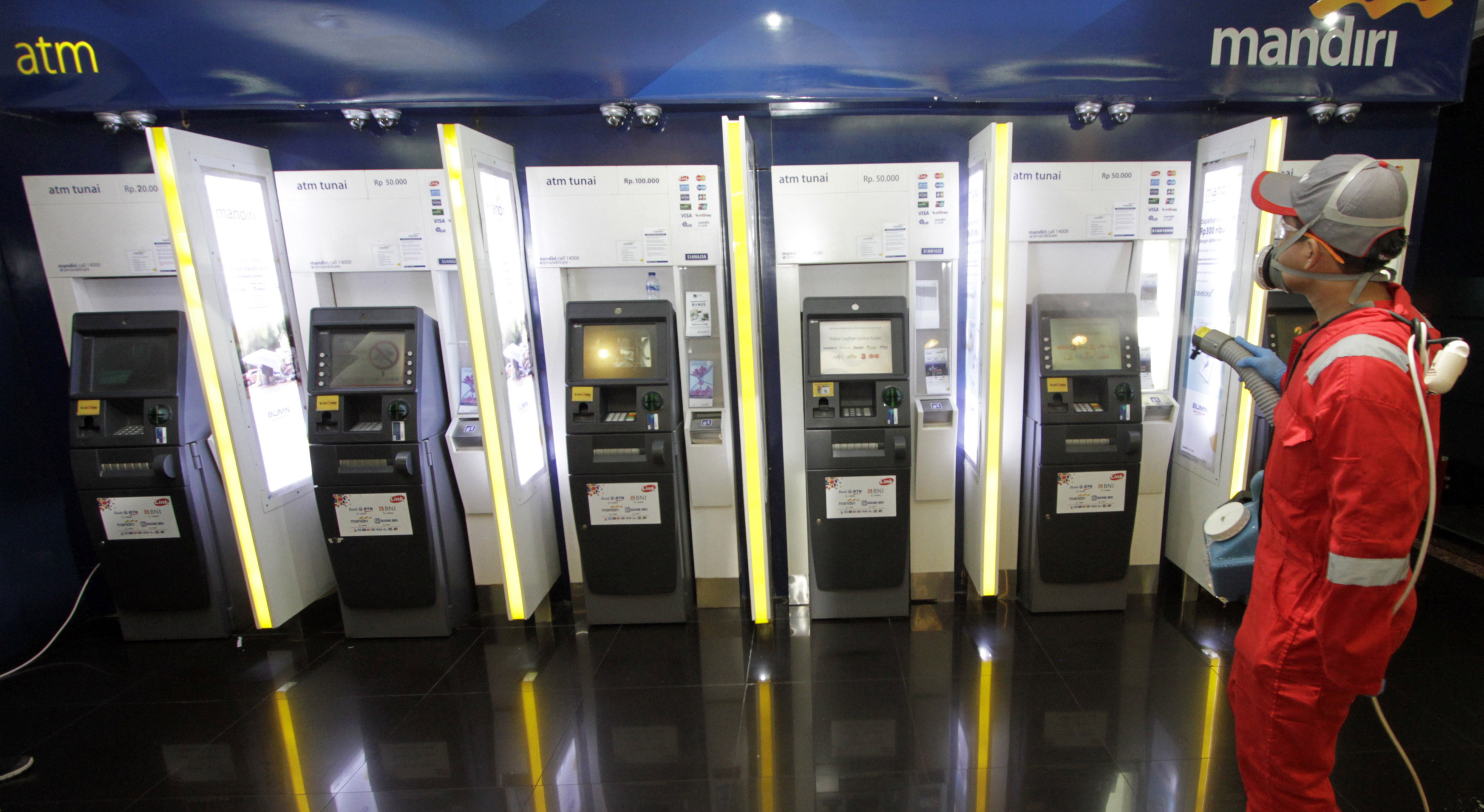 Petugas menyemprotkan disinfektan ke ruang ATM di Kantor Bank Mandiri Cabang Thamrin, Jakarta.