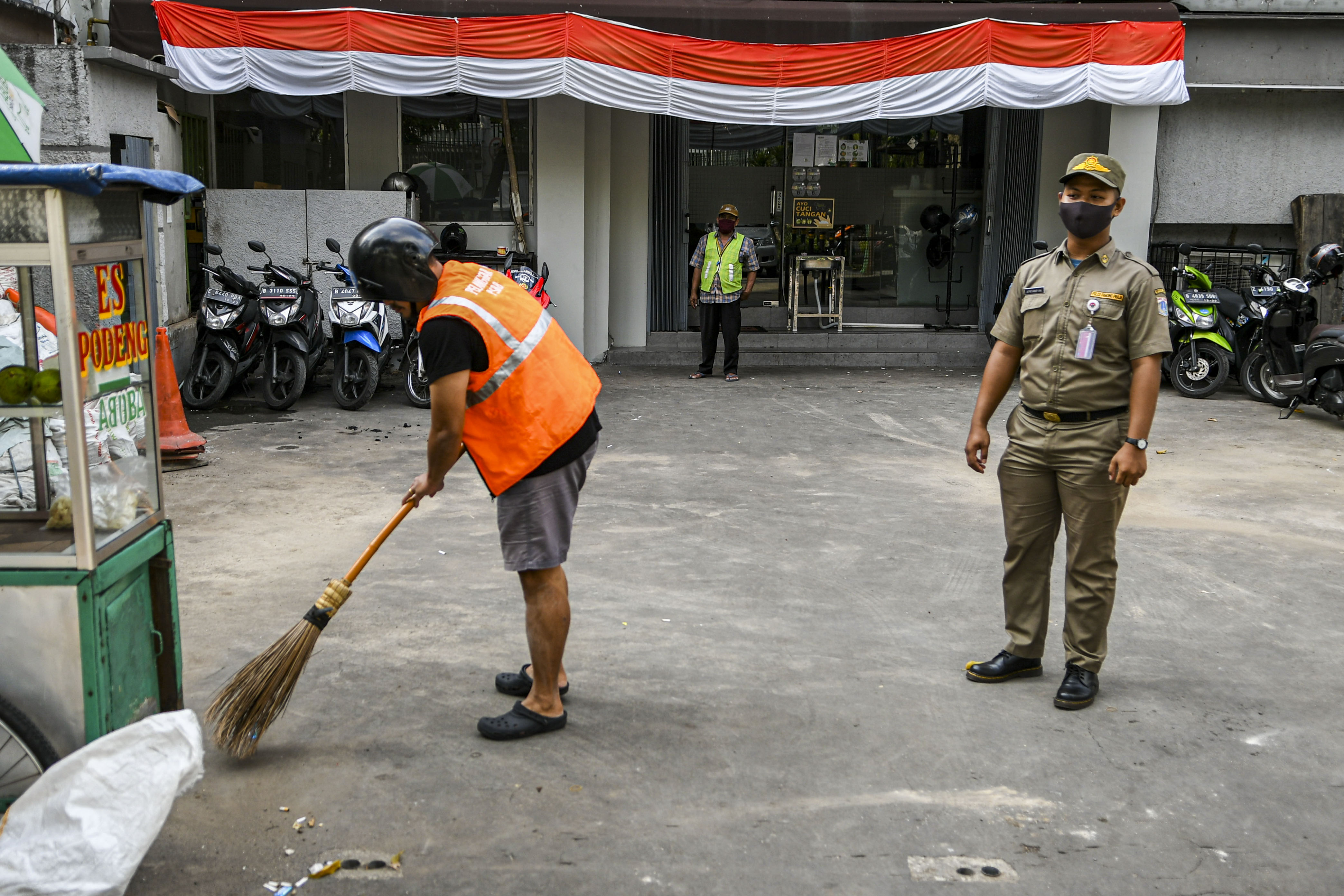 Petugas Satpol PP mengawasi pelanggar aturan PSBB melaksanakan sanksi kerja sosial dengan menyapu sampah di kawasan Sabang, Jakarta.