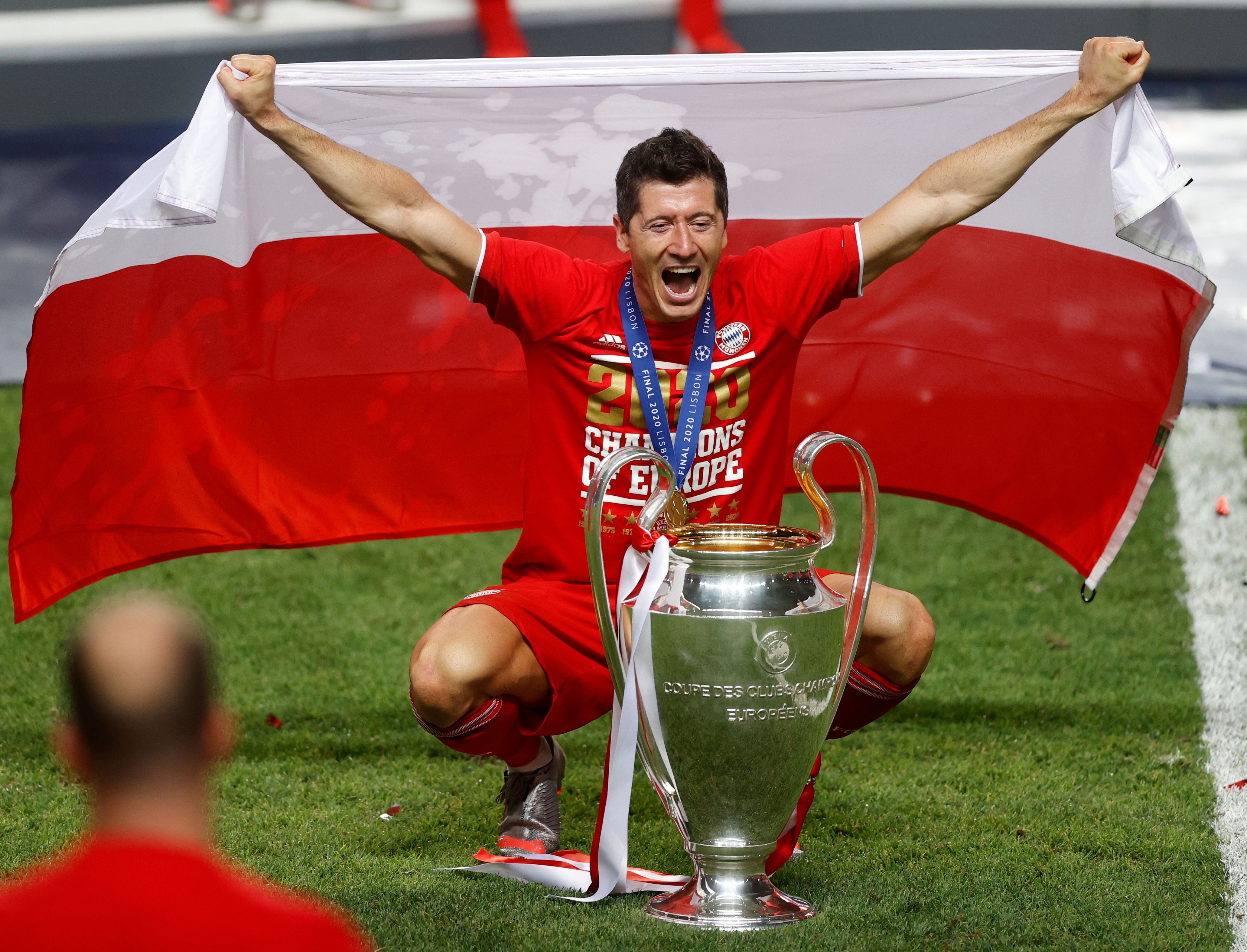 Robert Lewandowski berpose sambil memegang bendera Polandia dan piala Liga Champions.