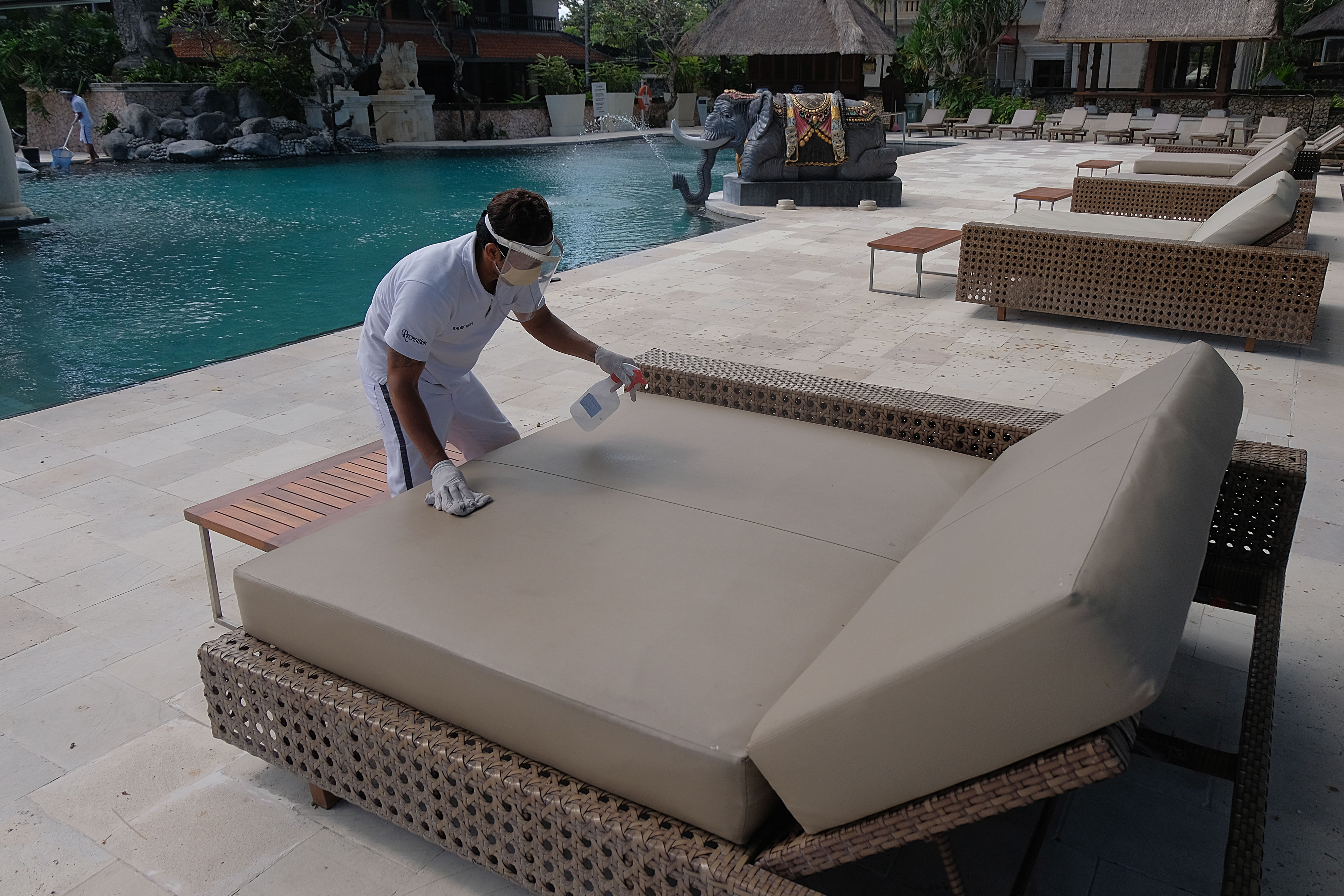 Pekerja menggunakan alat pelindung diri saat membersihkan tempat bersantai bagi wisatawan di Hotel Puri Santrian, Sanur, Denpasar