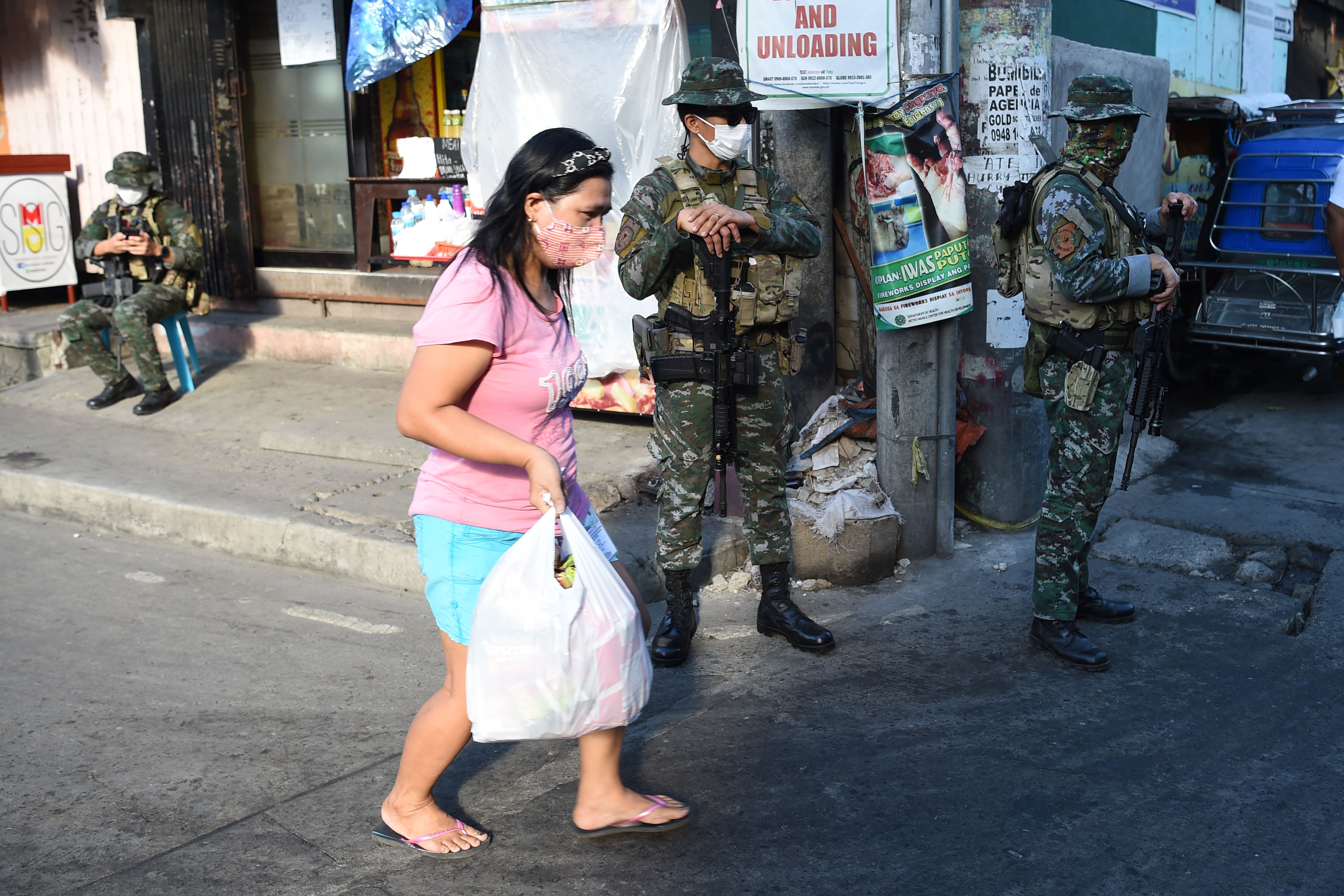 Seorang wanita berjalan melewati anggota polisi di sebuah pos pemeriksaan di pinggiran kota Manil pada 16 Juli 2020.