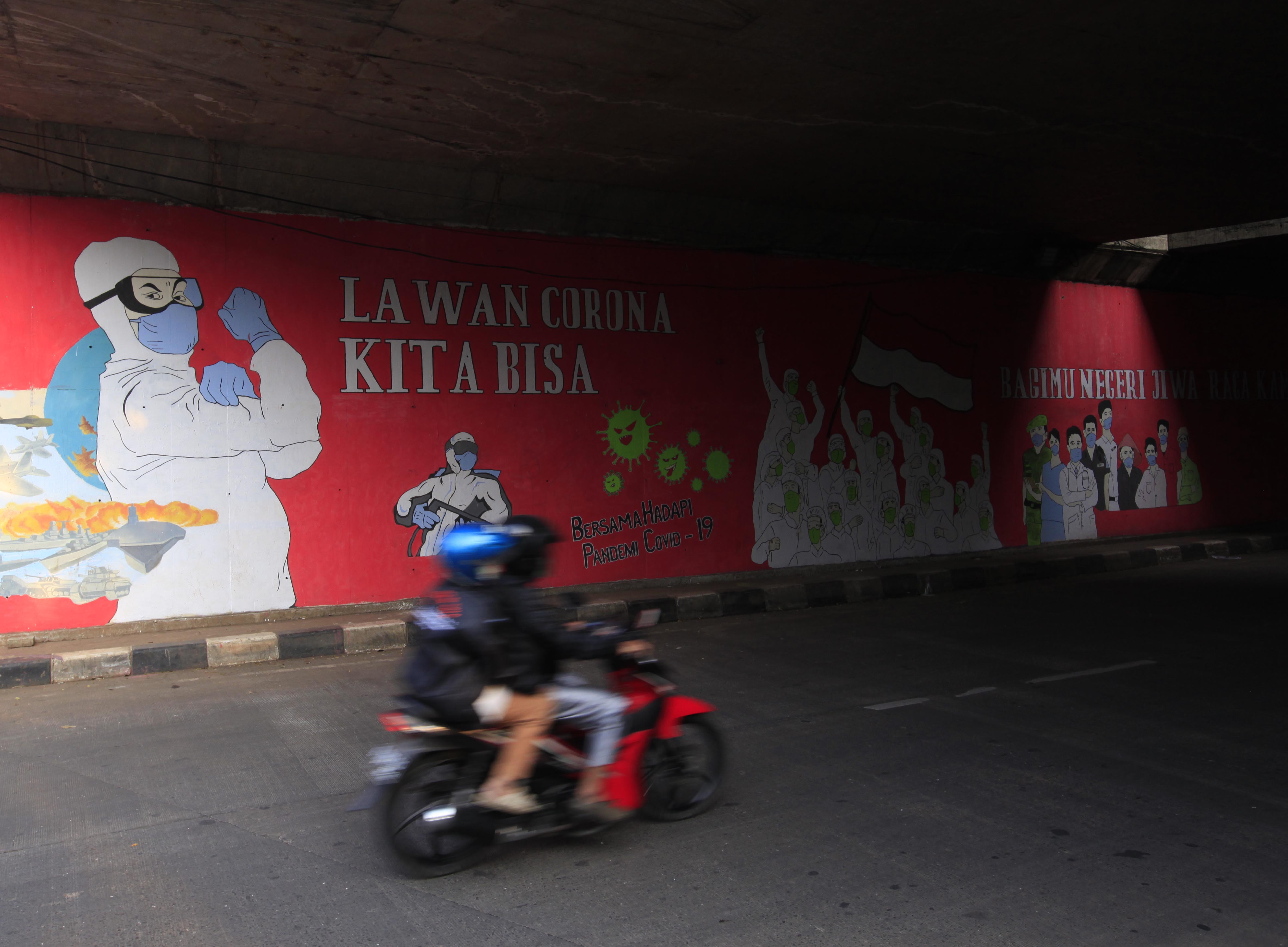  Pengendara motor melintasi di depan mural bertuliskan ajakan lawan covid-19 di Cilangkap, Jakarta Timur, Kamis (20/8/2020).
