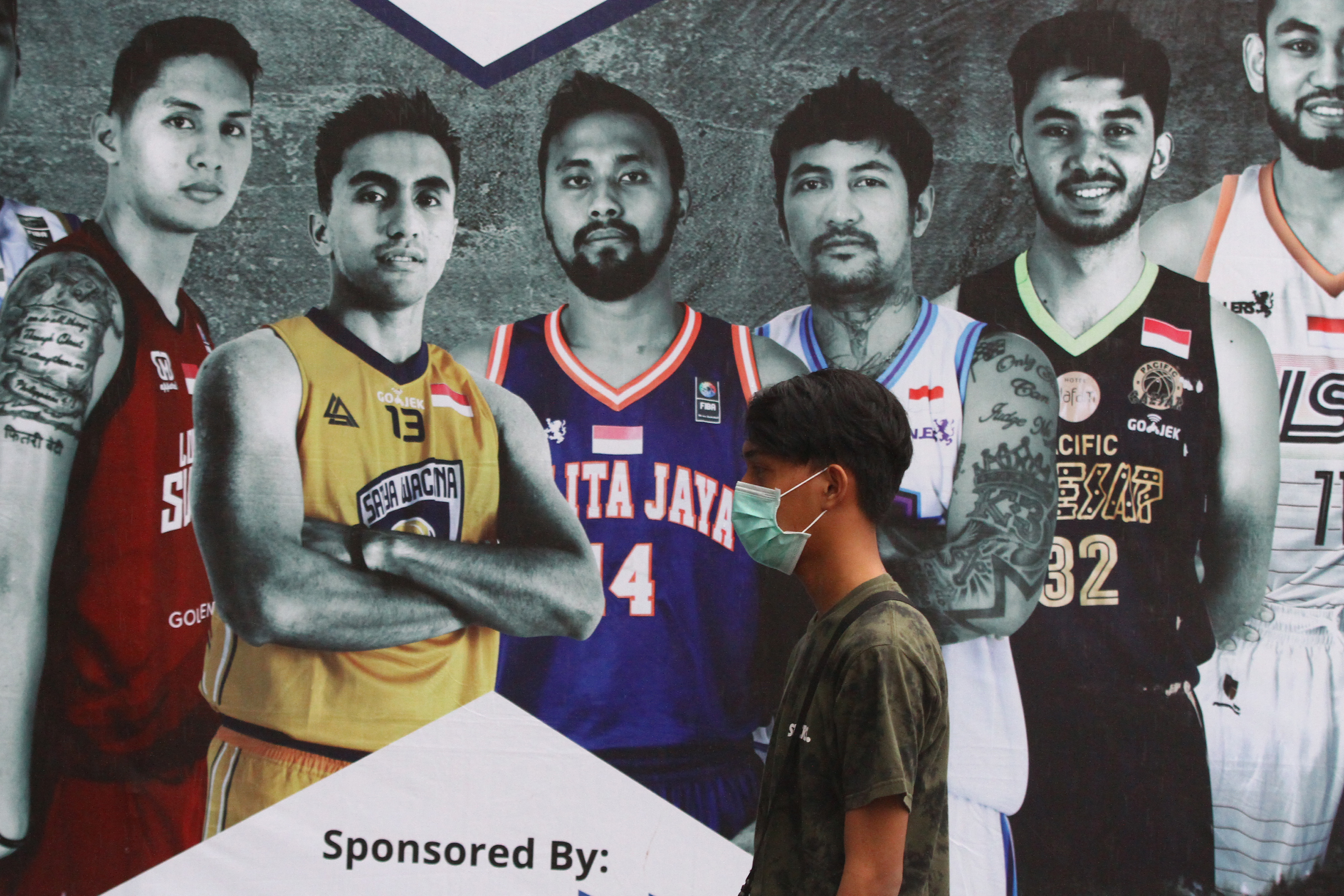 Seorang warga melintasi baliho kompetisi IBL 2020 di Malang, Jawa Tengah.