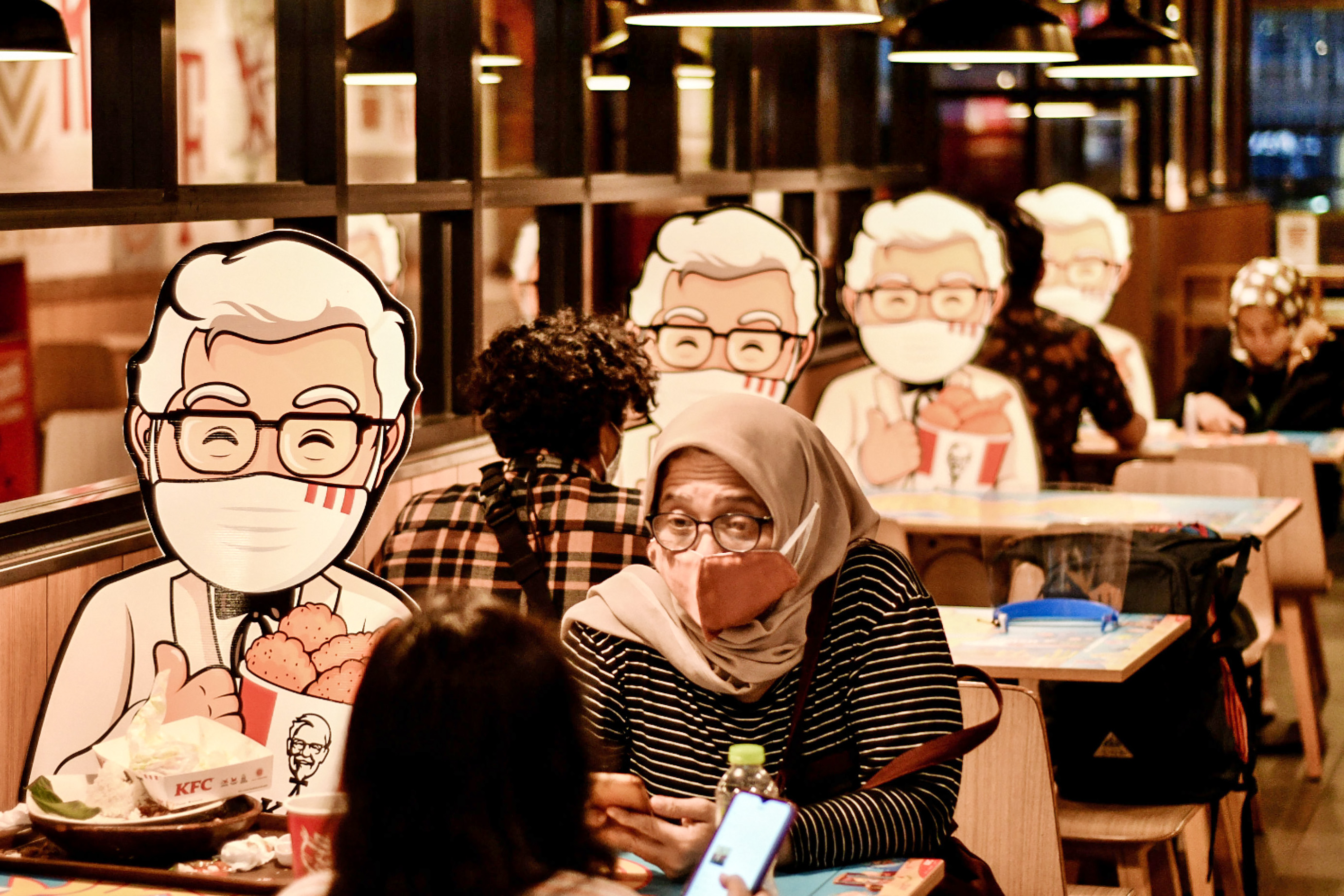 Pengunjung duduk di antara meja yang dipasangi ‘mock-up’ maskot di salah satu restoran cepat saji di kawasan Pancoran, Jakarta.