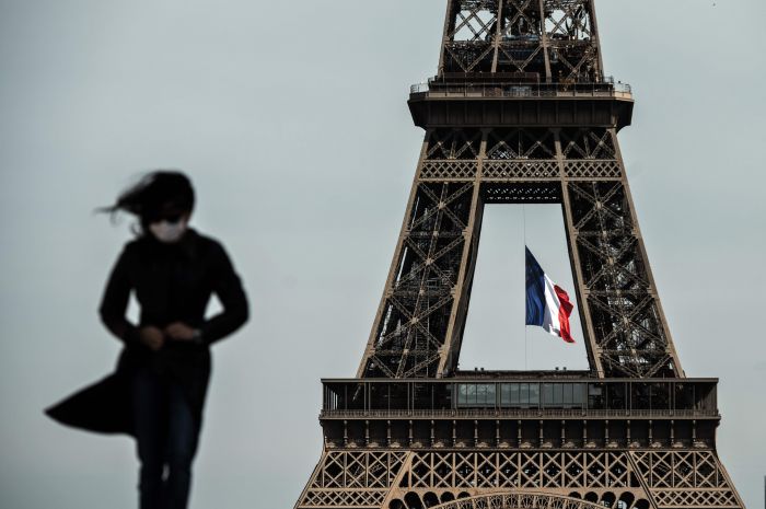 Seorang warga Paris memakai masker berjalan di sekitar Menara Eiffel Paris. Kasius covid-19 di negara itu melonjak tinggi.