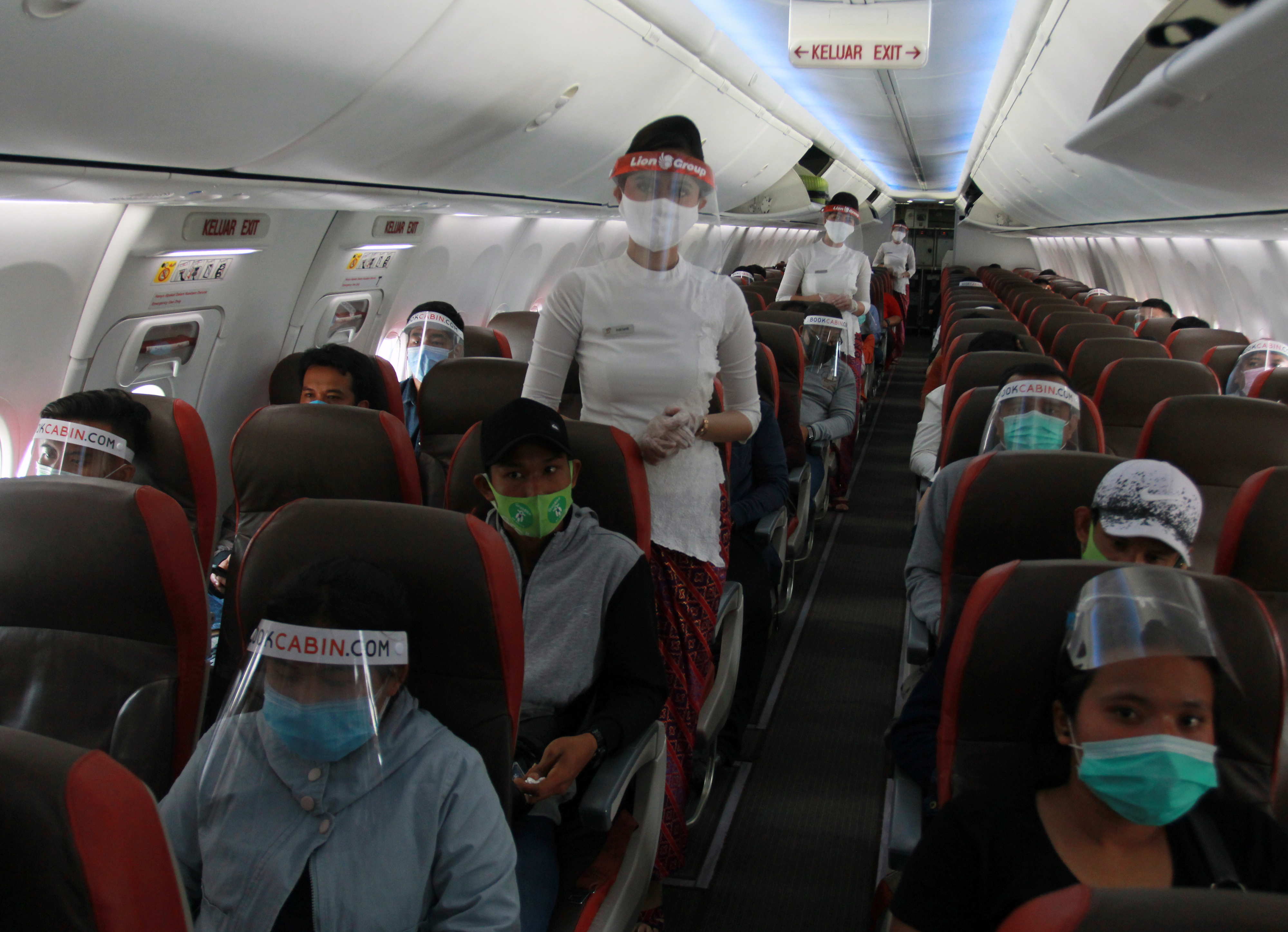  Kru pesawat dengan menggunakan alat pelindung wajah dan sarung tangan menyambut kedatangan penumpang di dalam pesawat 