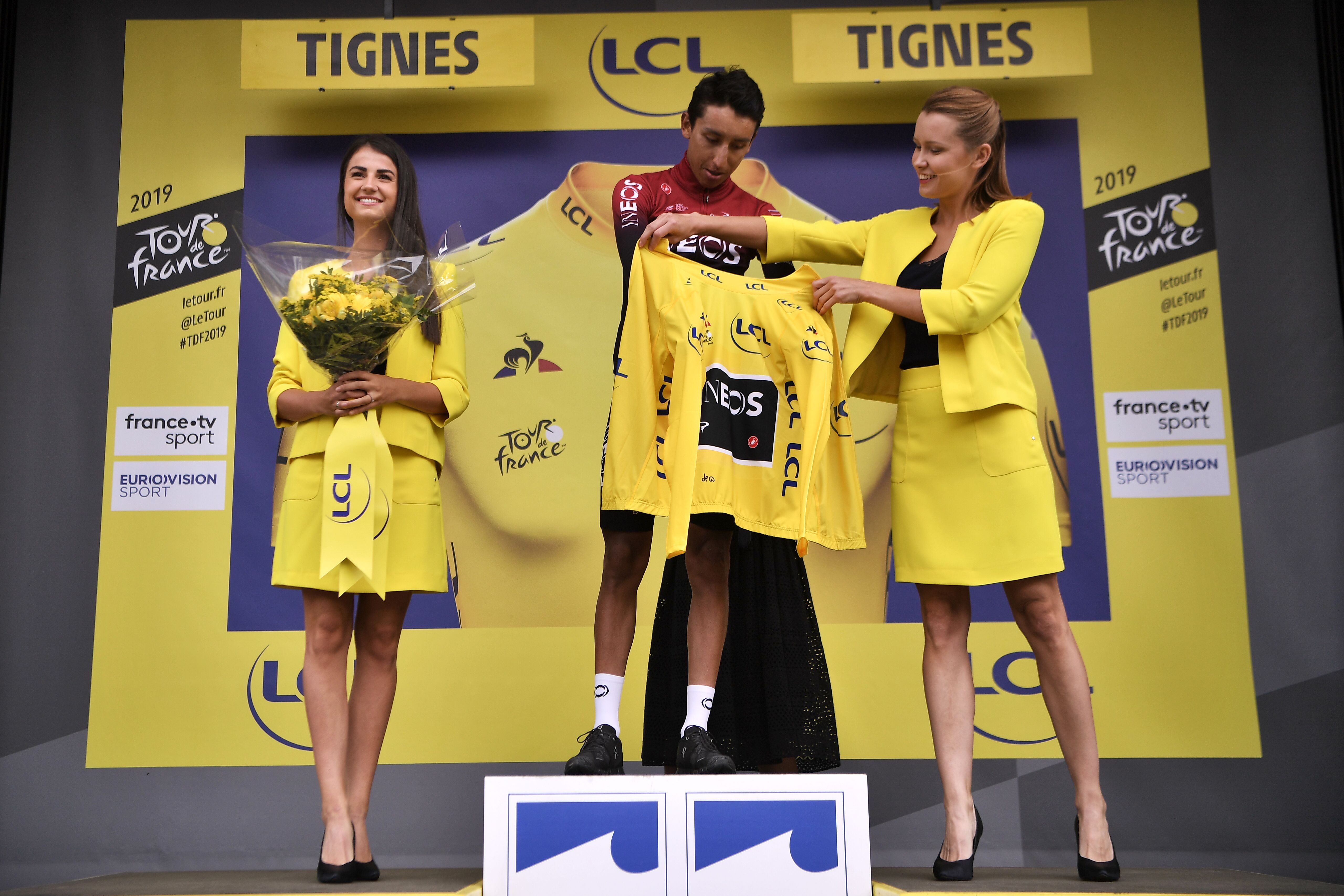 Dua podium girl mengapit Egan Bernal yang memenangi etape ke-19 Tour de France 2019.