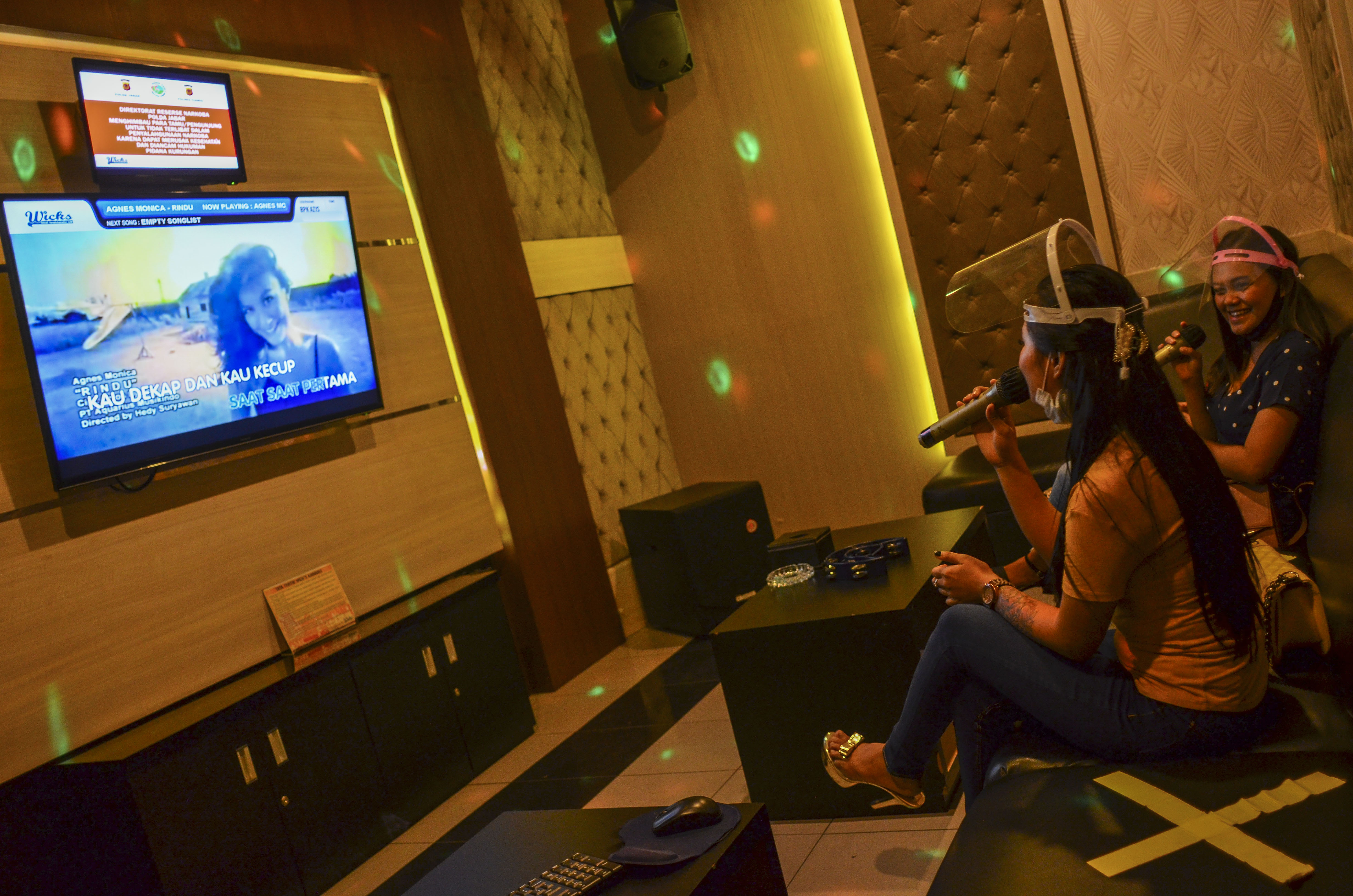  Pengunjung bernyanyi dengan menerapkan jaga jarak di sebuah gerai karaoke