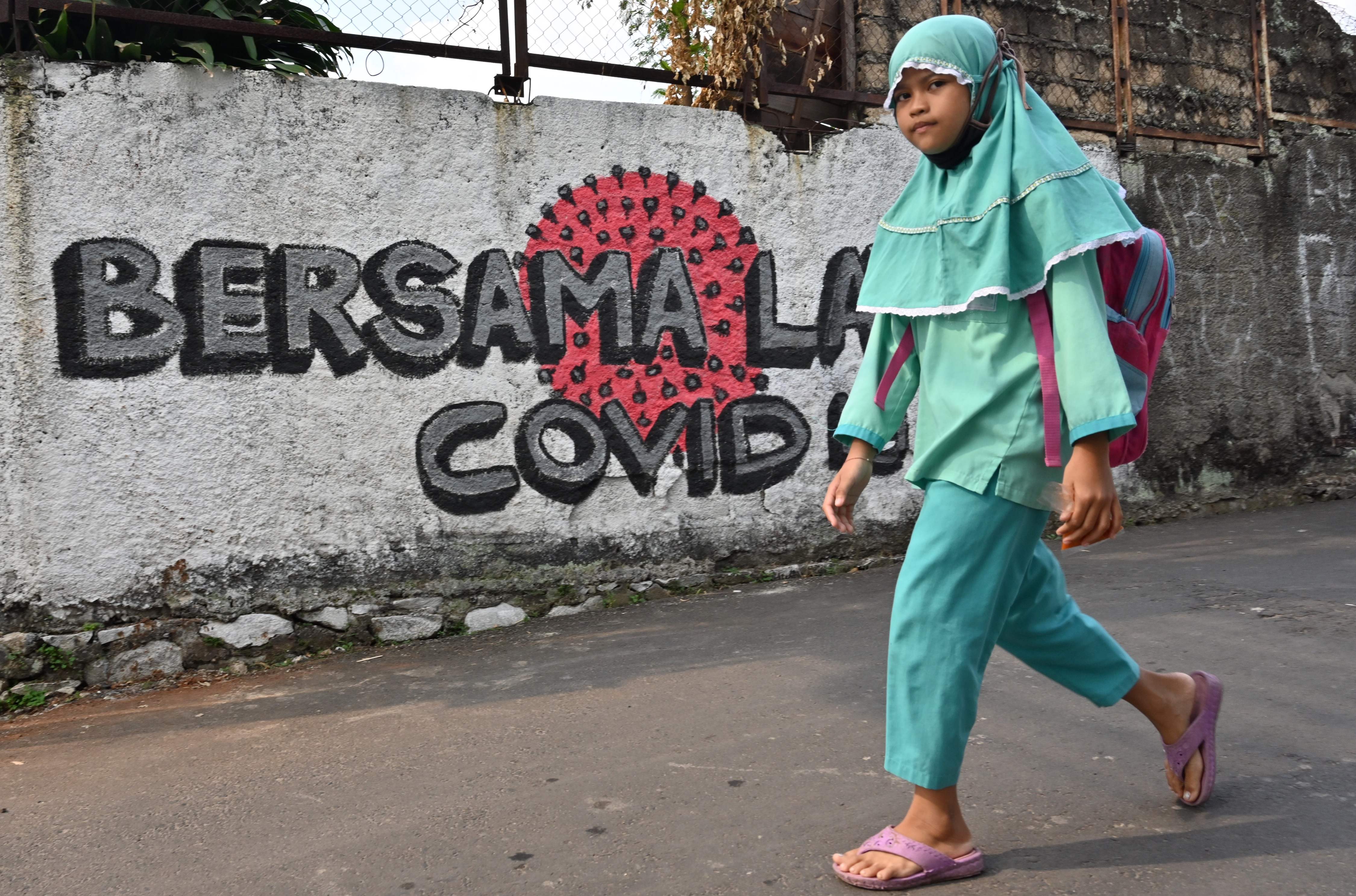 Seorang anak melintasi mural kampanye covid-19 di Jakarta.