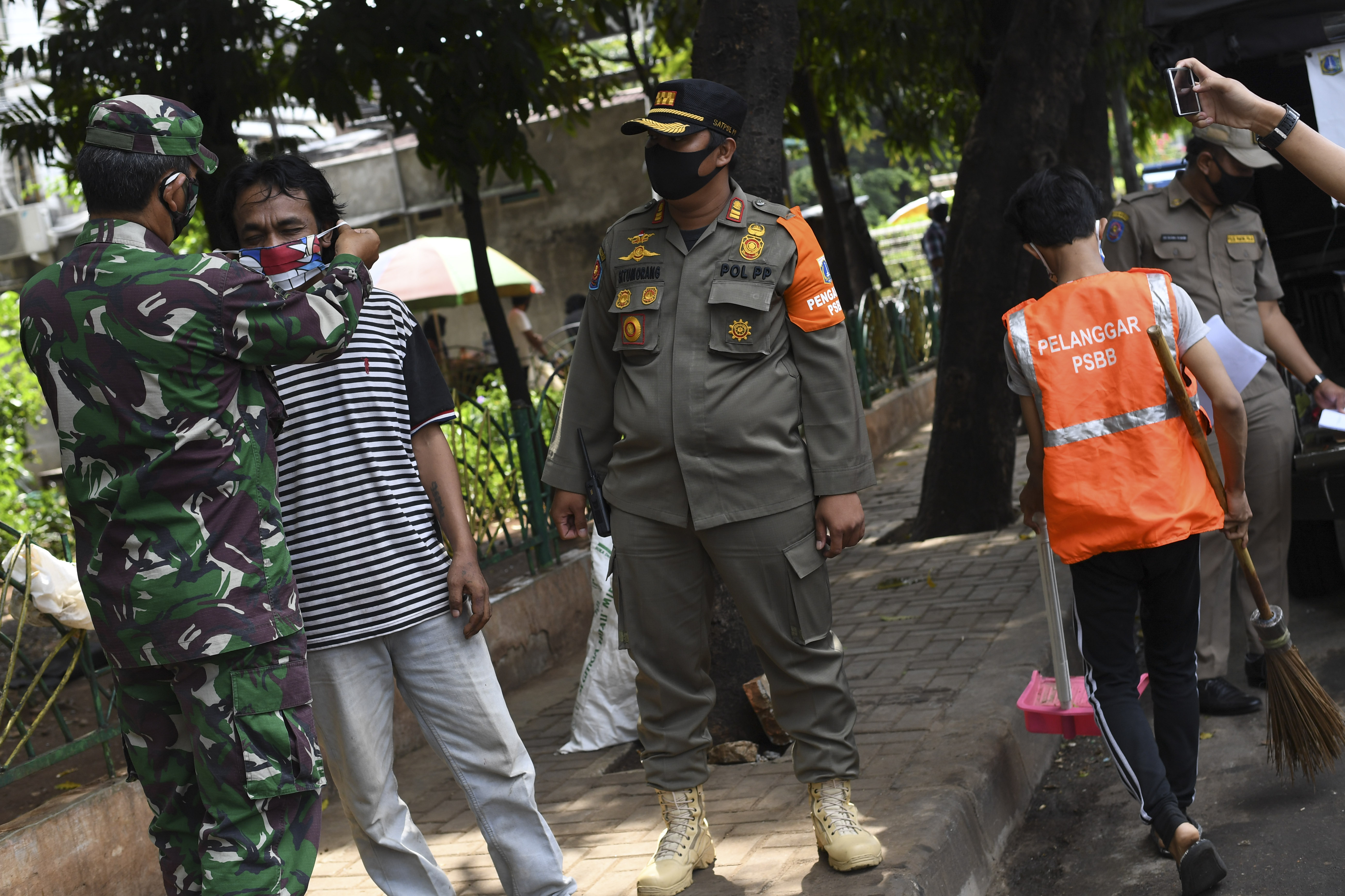 Petugas gabungan memasangkan masker dan memberi hukuman menyapu jalan bagi warga yang tidak mengenakan masker di Jakarta, Selasa (7/7/2020).
