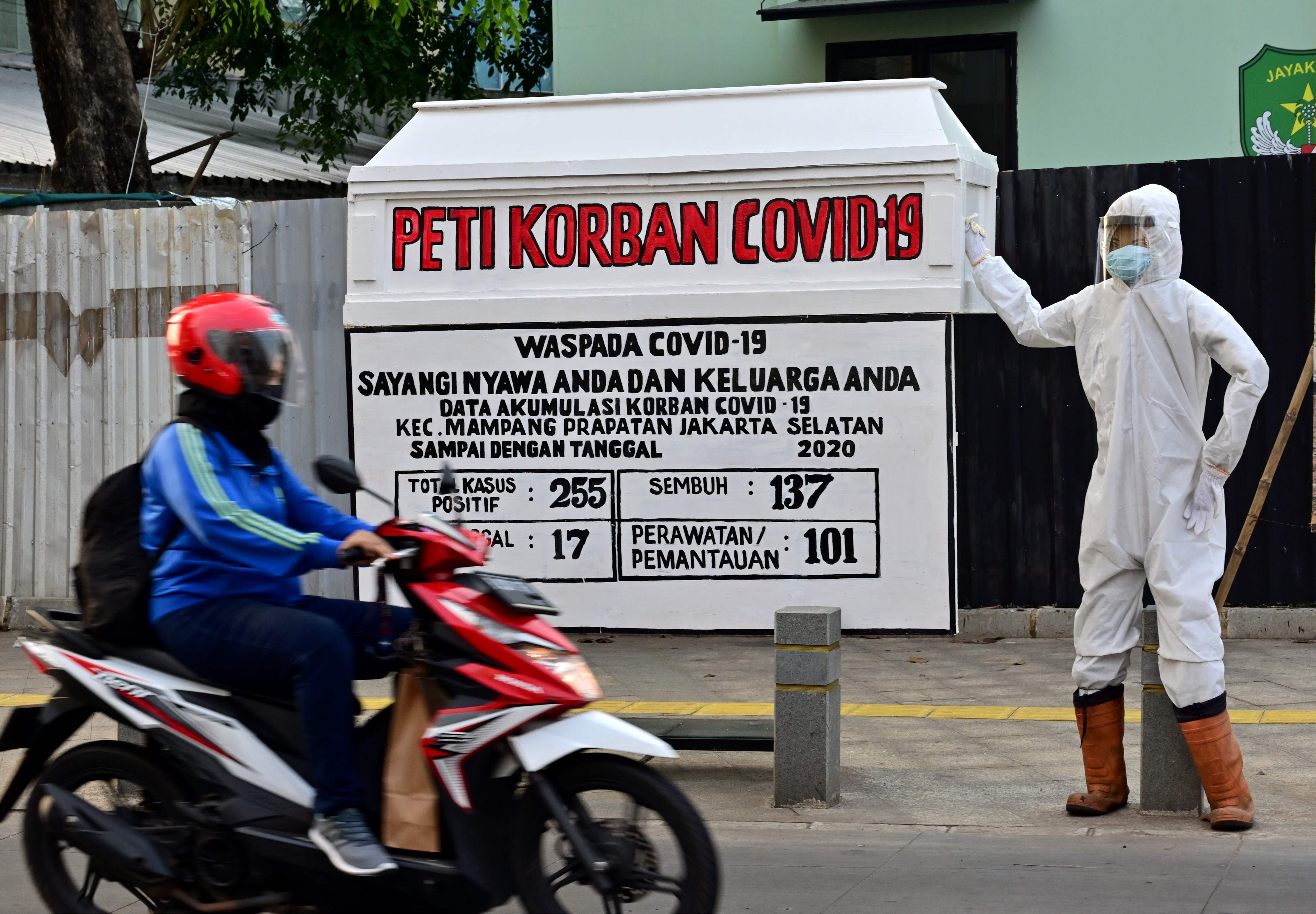 Seorang warga melintas di depan instalasi yang menampilkan peti jenazah, petugas mengenakan APD, dan data statistik covid-19 di Jakarta.