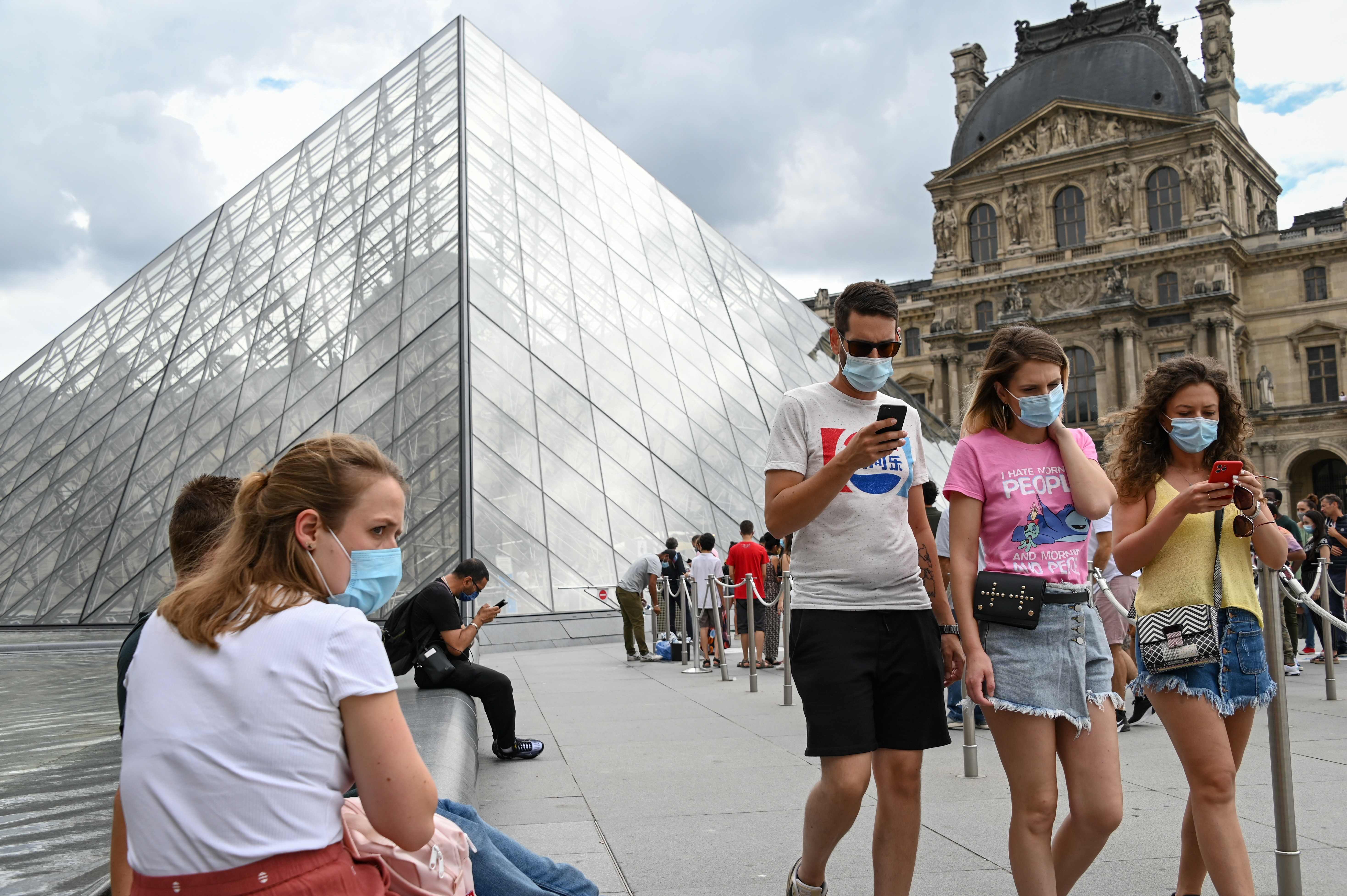 Warga mengenakan masker melintas di depan Pyramide du Louvre di Paris, Prancis.