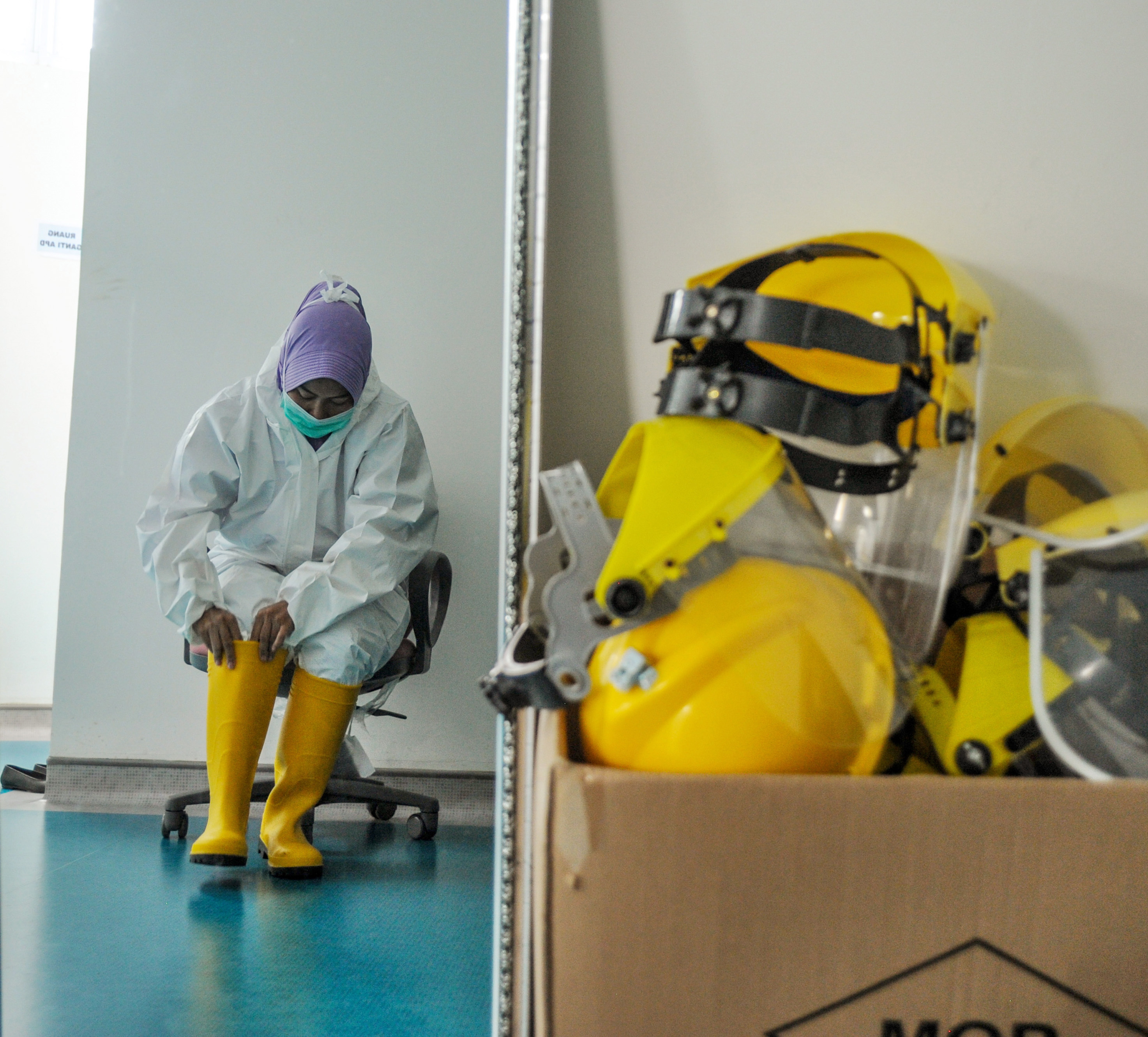 Seorang tenaga kesehatan memakai alat pelindung diri sebelum memberikan makanan kepada pasien positif COVID-19.