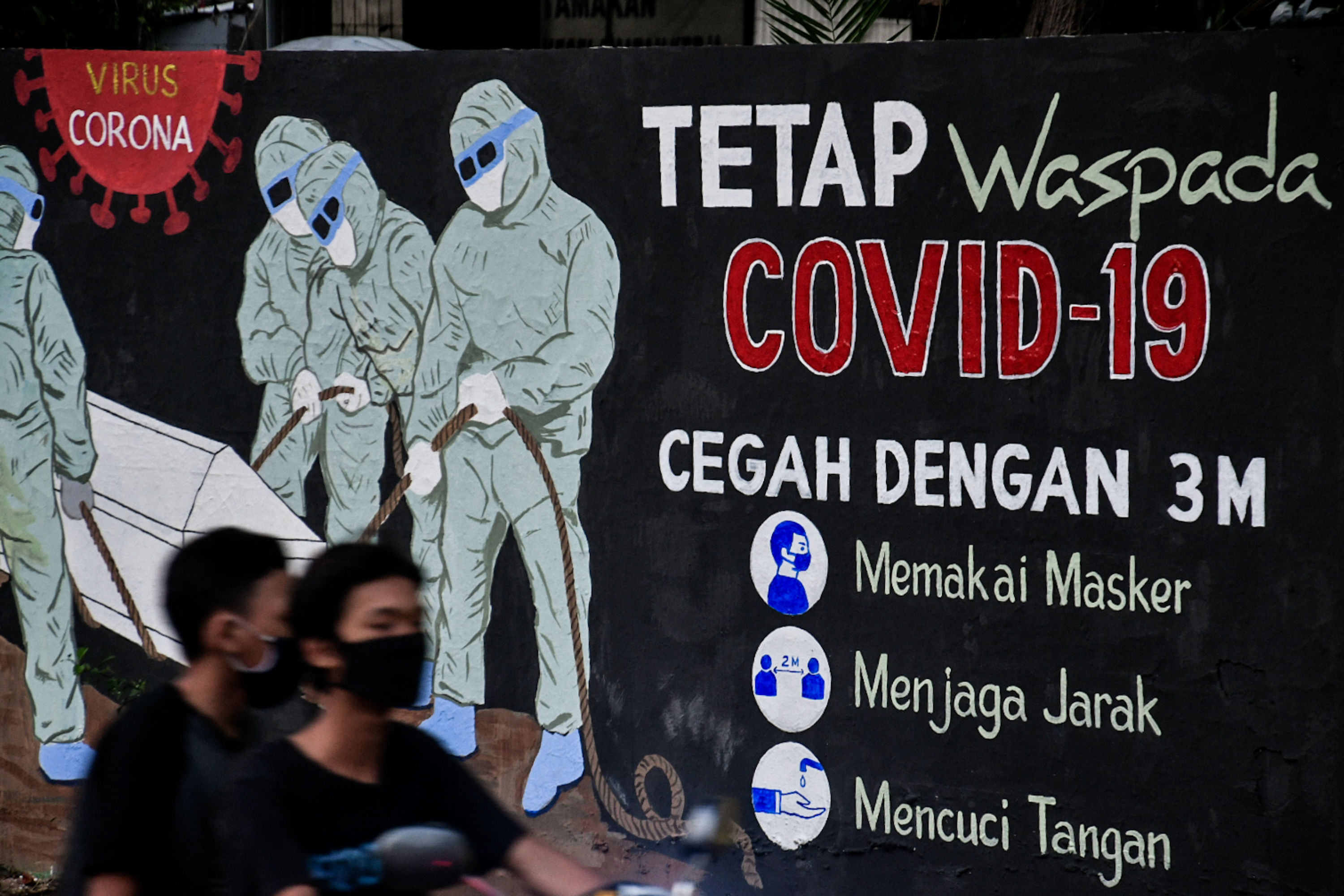 Pengendara melintasi mural terkait covid-19 di wilayah Tebet, Jakarta.