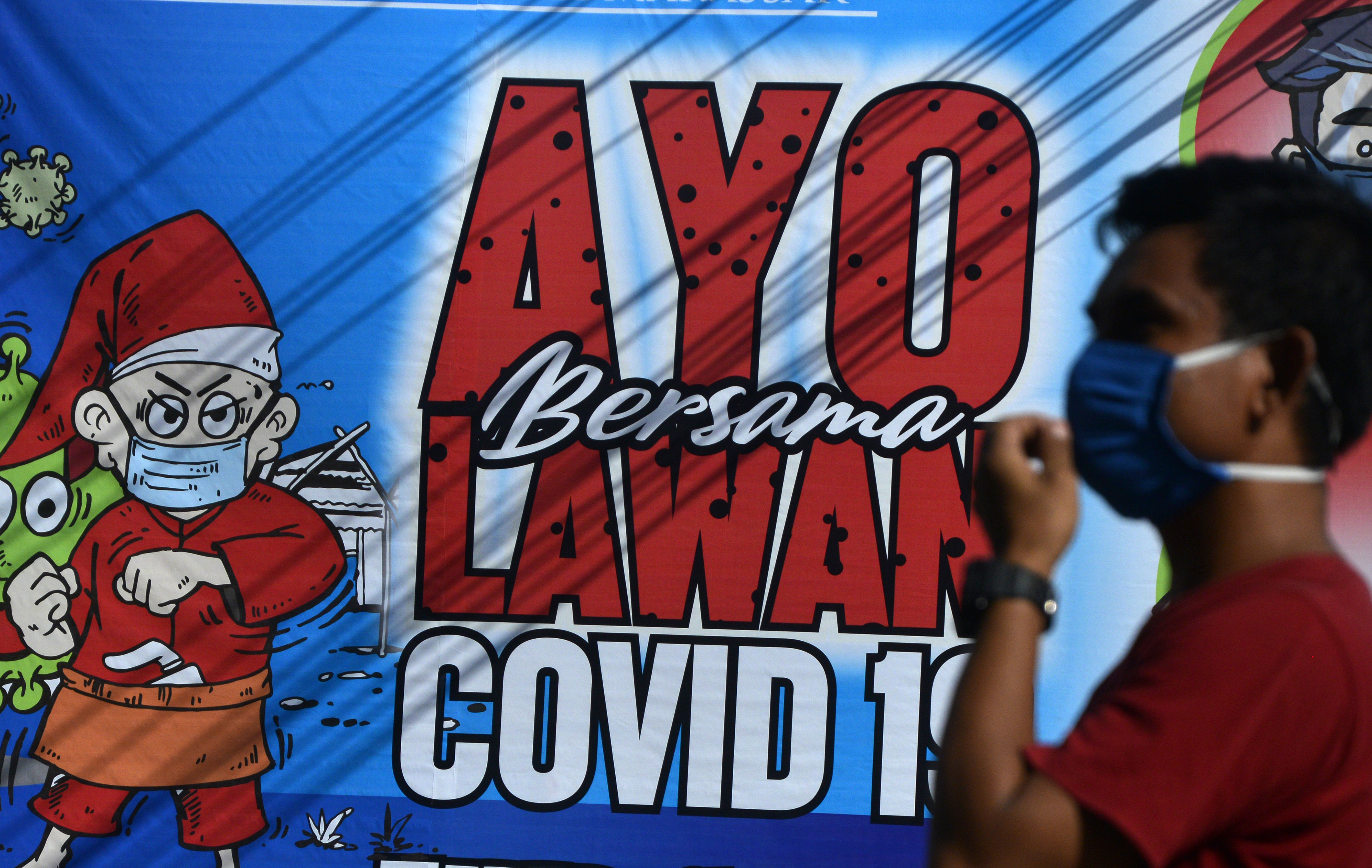 Warga melintas di spanduk imbauan untuk bersama-sama melawan Covid-19