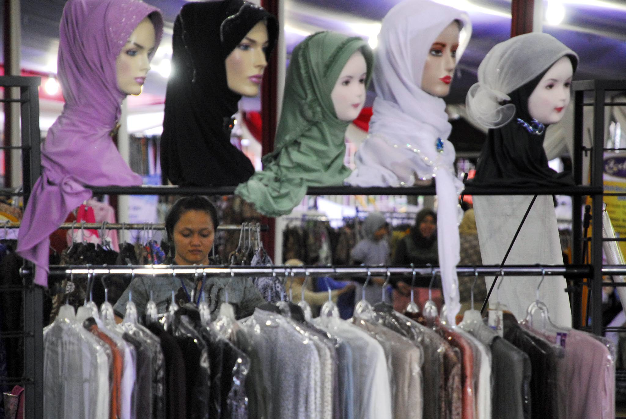 Seorang perempuan berada di depan deretan busana muslim dan jilbab yang dipajang di sebuah stan arena.