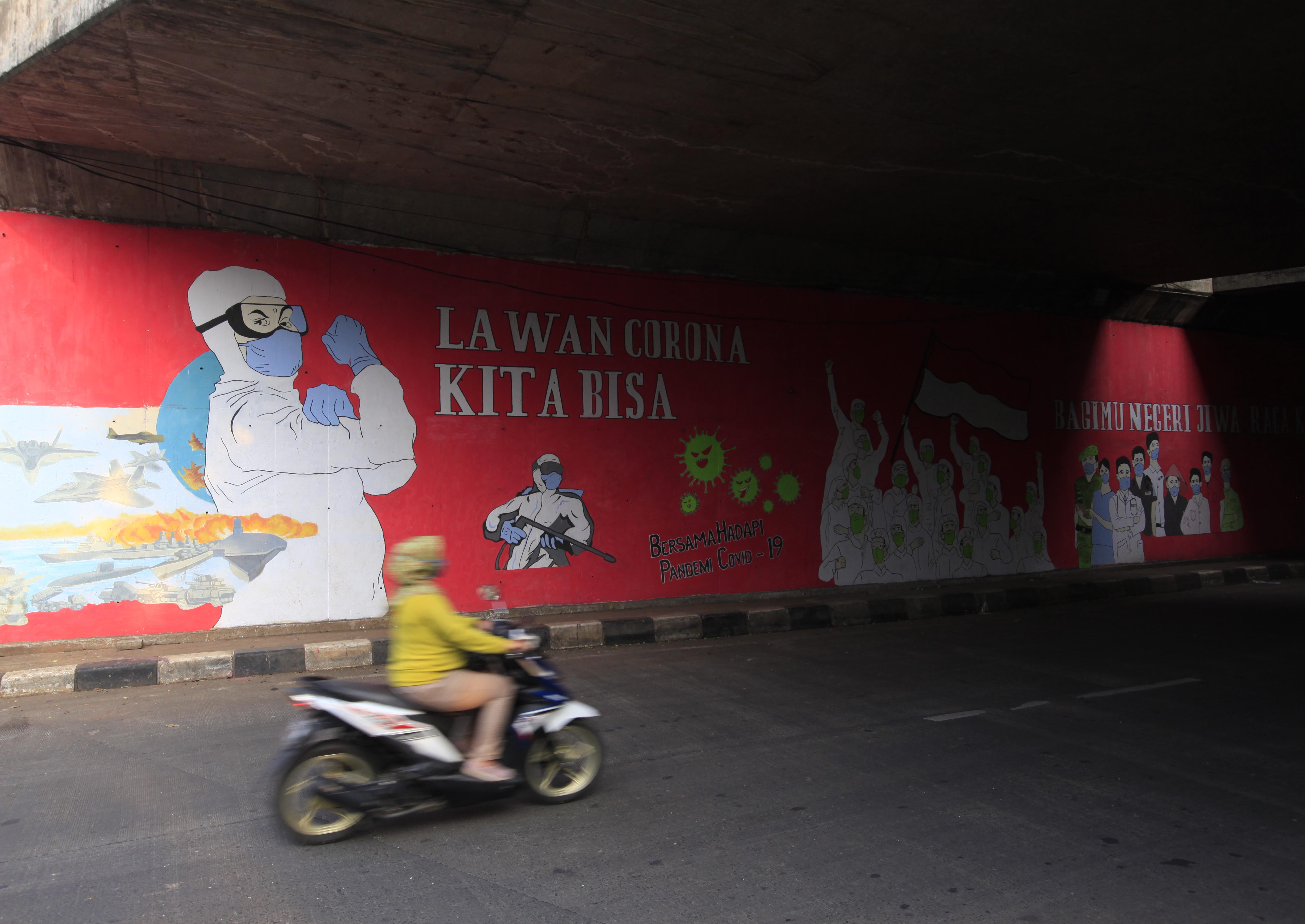  Pengendara motor melintasi mural untuk melawan pandemi virus covid 19 di Cilangkap, Jakarta Timur, Kamis (20.8).