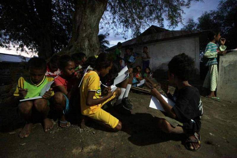 Anak-anak di Kecamatan Mapitara belajar berkelompok di luar rumah dengan mengandalkan penerangan sinar matahari sore hari. 