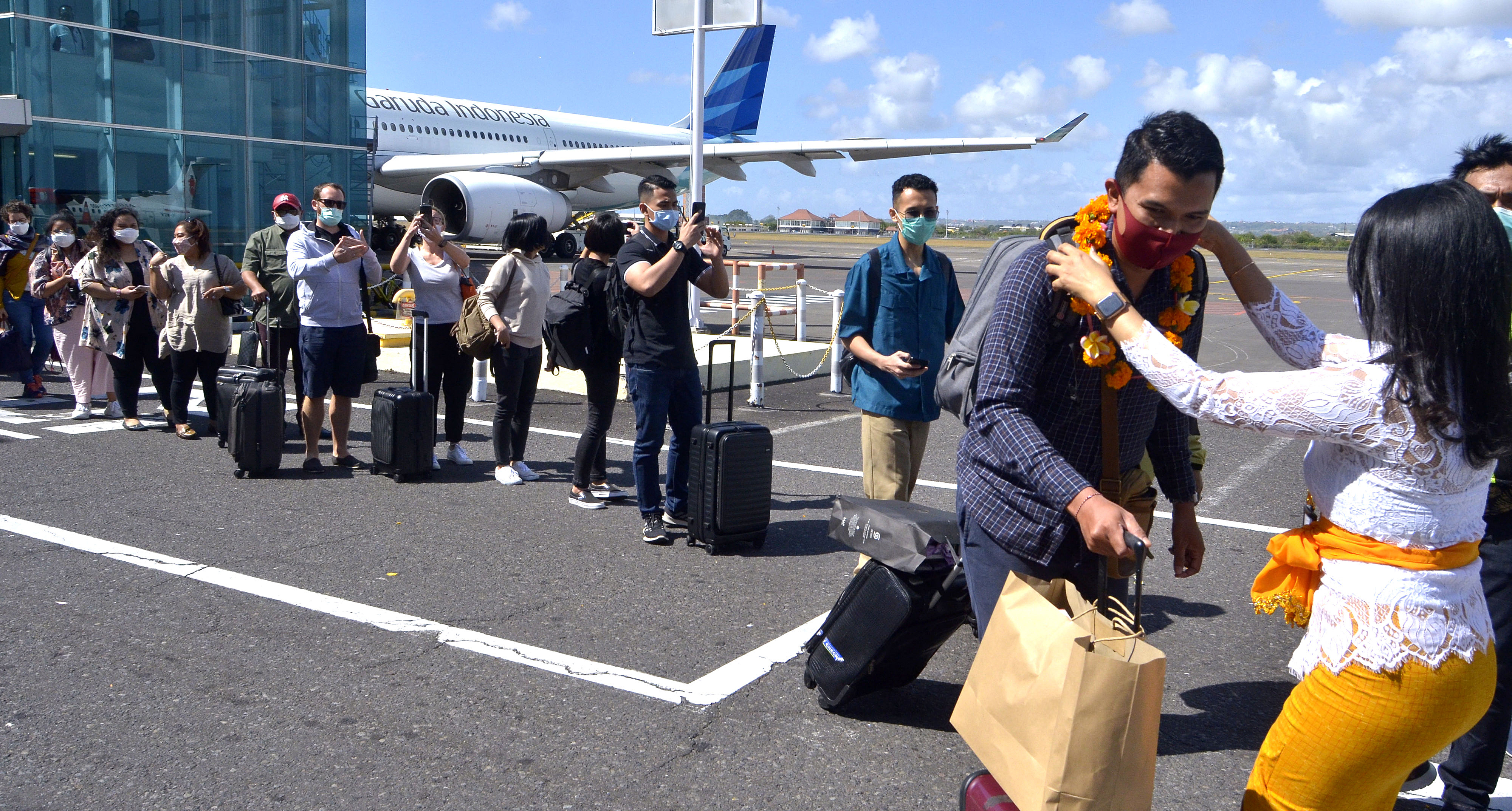 Petugas mengalungkan bunga menyambut penumpang pesawat rute domestik  tiba di Bandara  I Gusti Ngurah Rai, Bali, Jumat (31/7/2020).