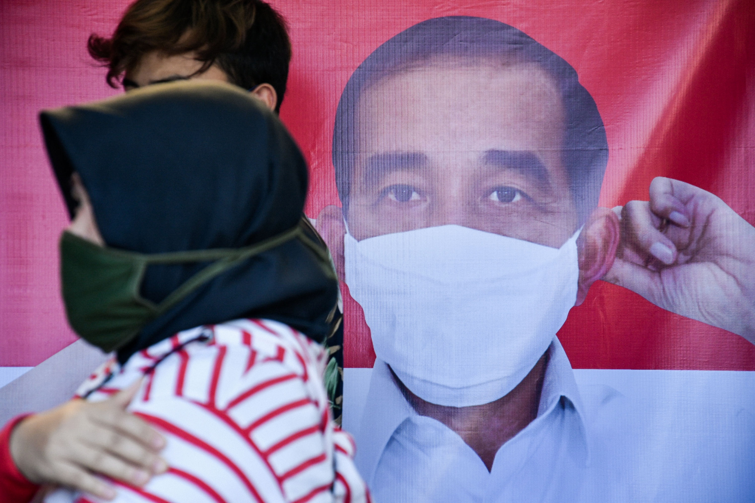 Warga melintasi foto Presiden Jokowi yang menggunakan masker di kawasan Tanah Abang, Jakarta.