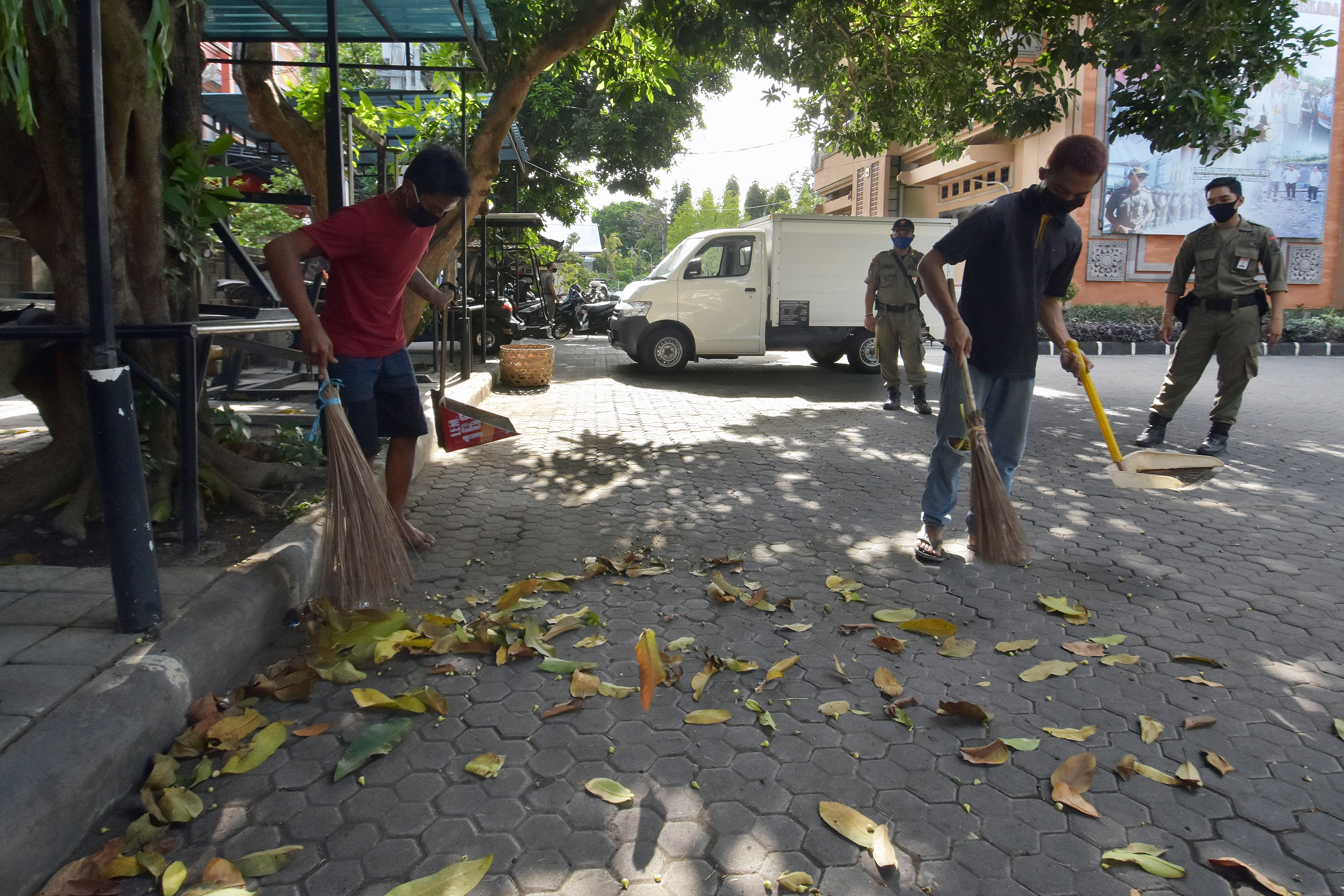 RAZIA : Dua warga yang melanggar protokol kesehatan menjalani sanksi sosial dengan menyapu halaman kantor Satpol PP Denpasar