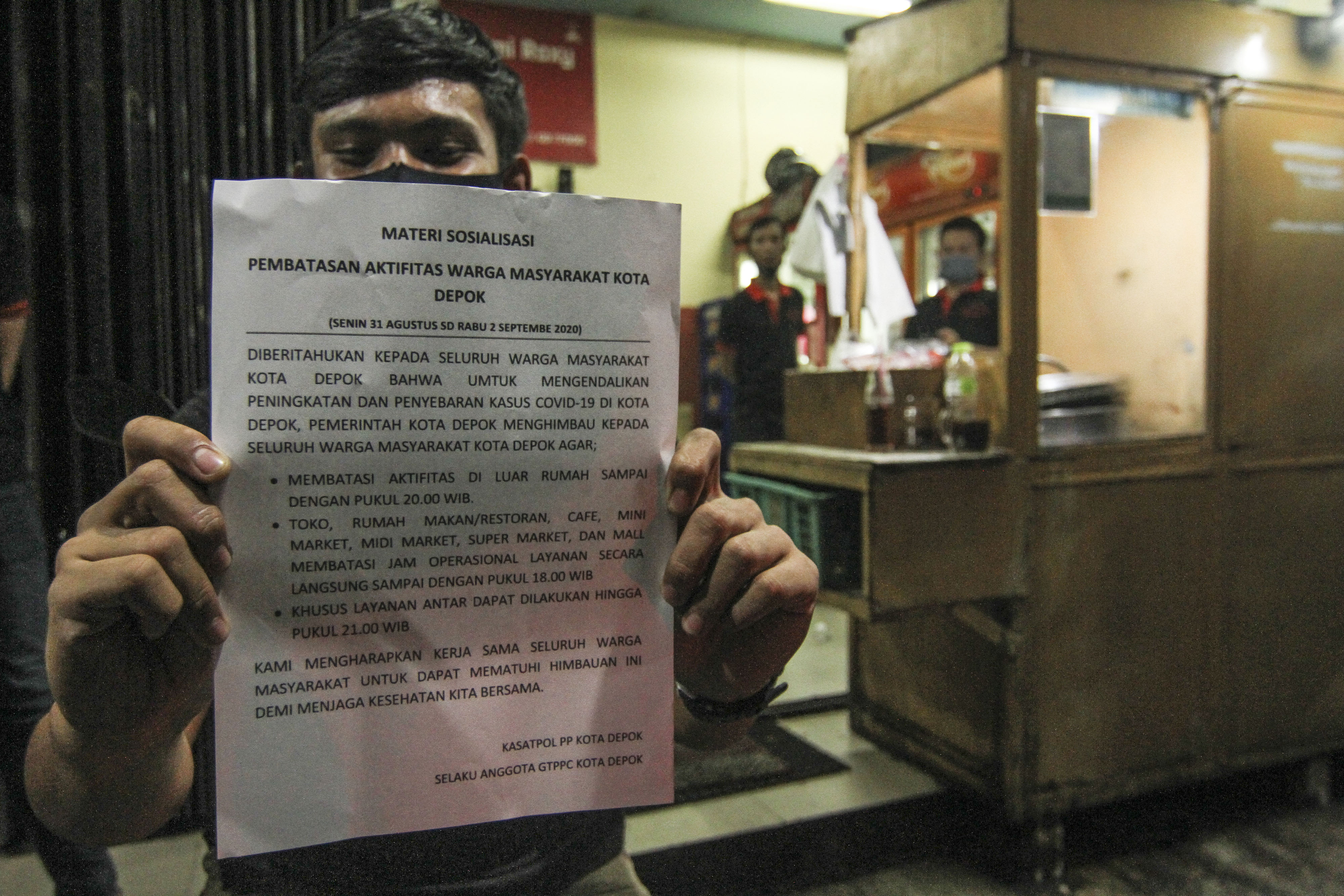 Pedagang di Depok menunjukkan pengumuman pemberlakukan jam malam