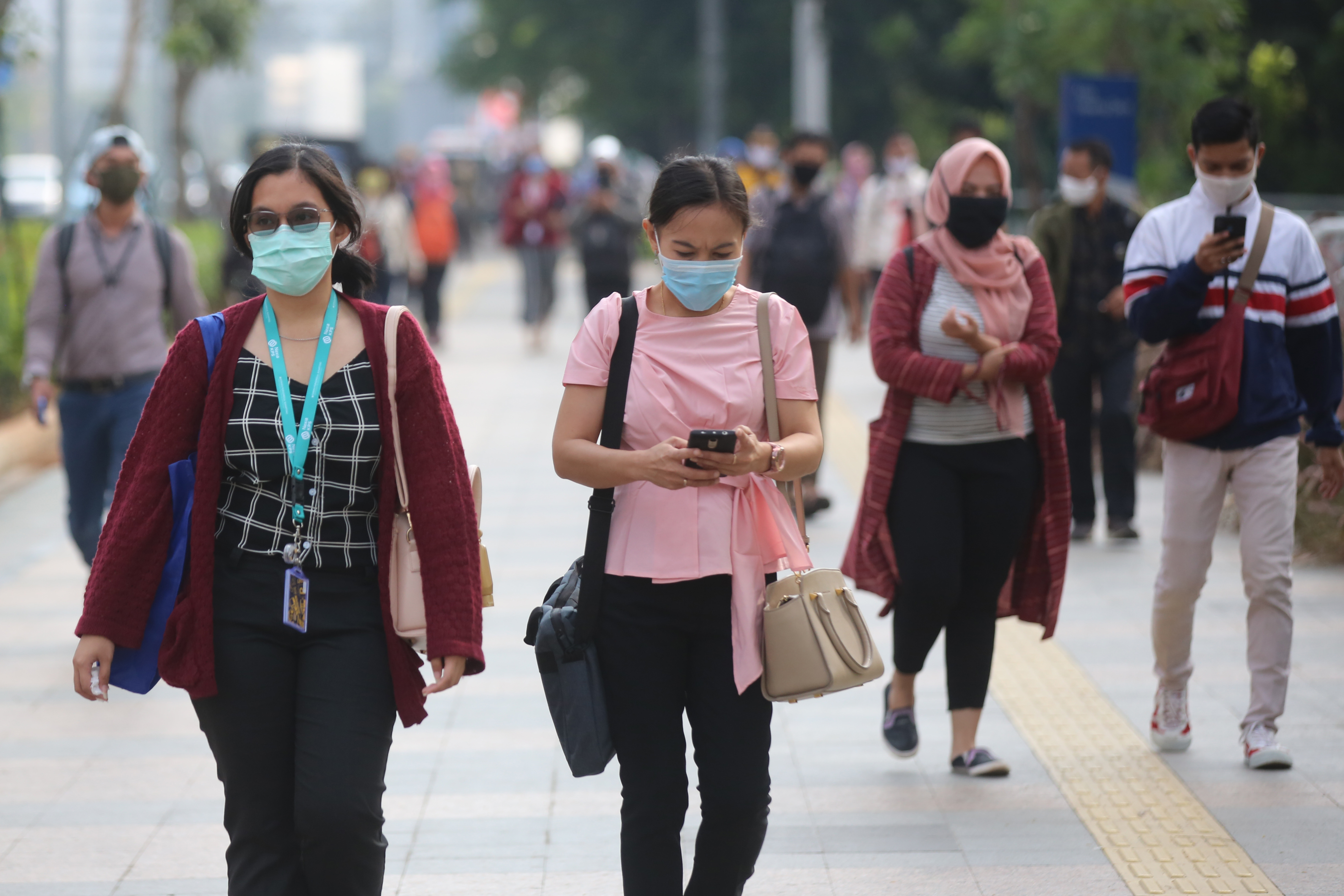 Pekerja menggunakan masker menuju kantor mereka melewati trotoar di kawasan Sudirman, Jakarta.