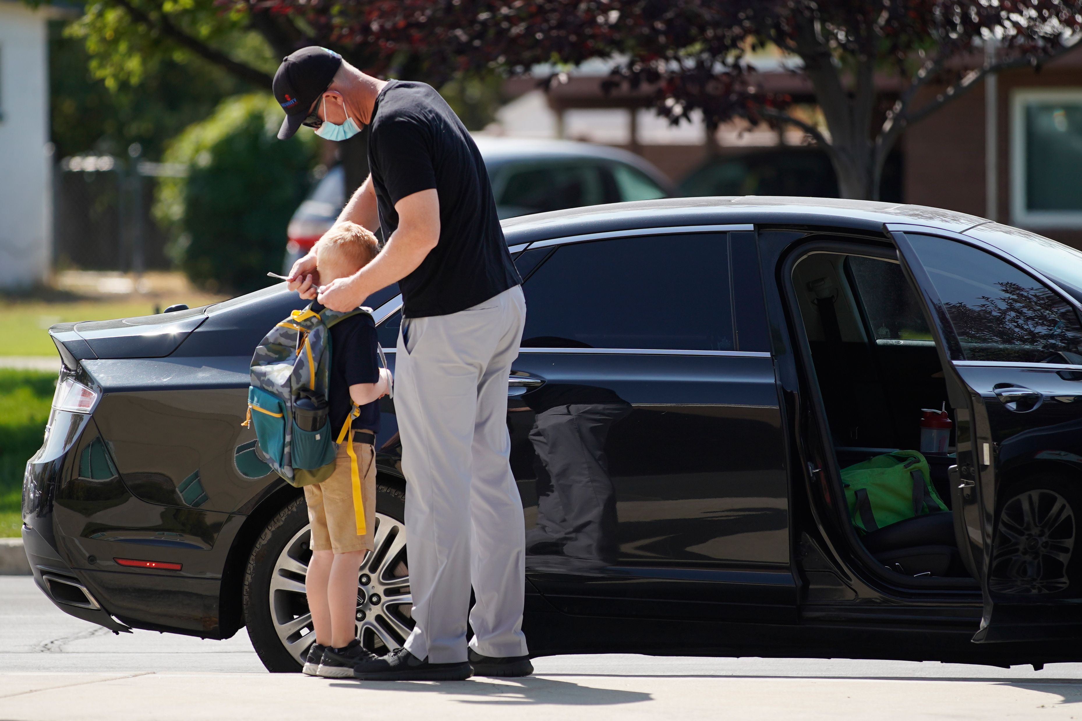 Seorang ayah mengenakan masker pada anaknya saat menurunkannya di sekolah di Provo, Utah, Amerika Serikat.