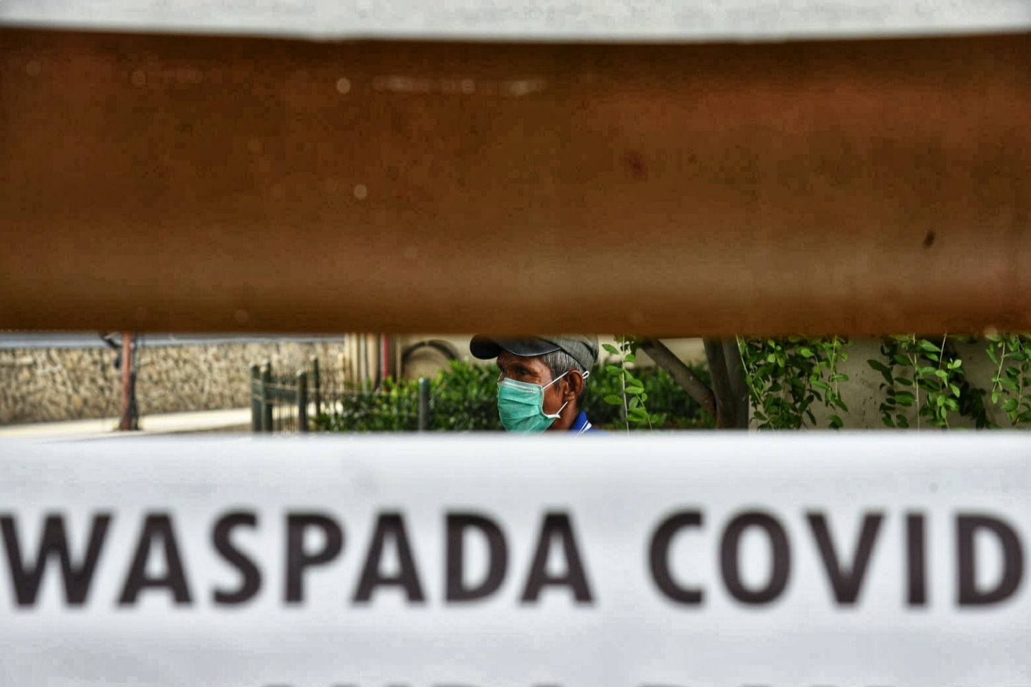 Pedagang yang melintasi papan imbauan waspada covid-19 di kawasan Sudirman, Jakarta.