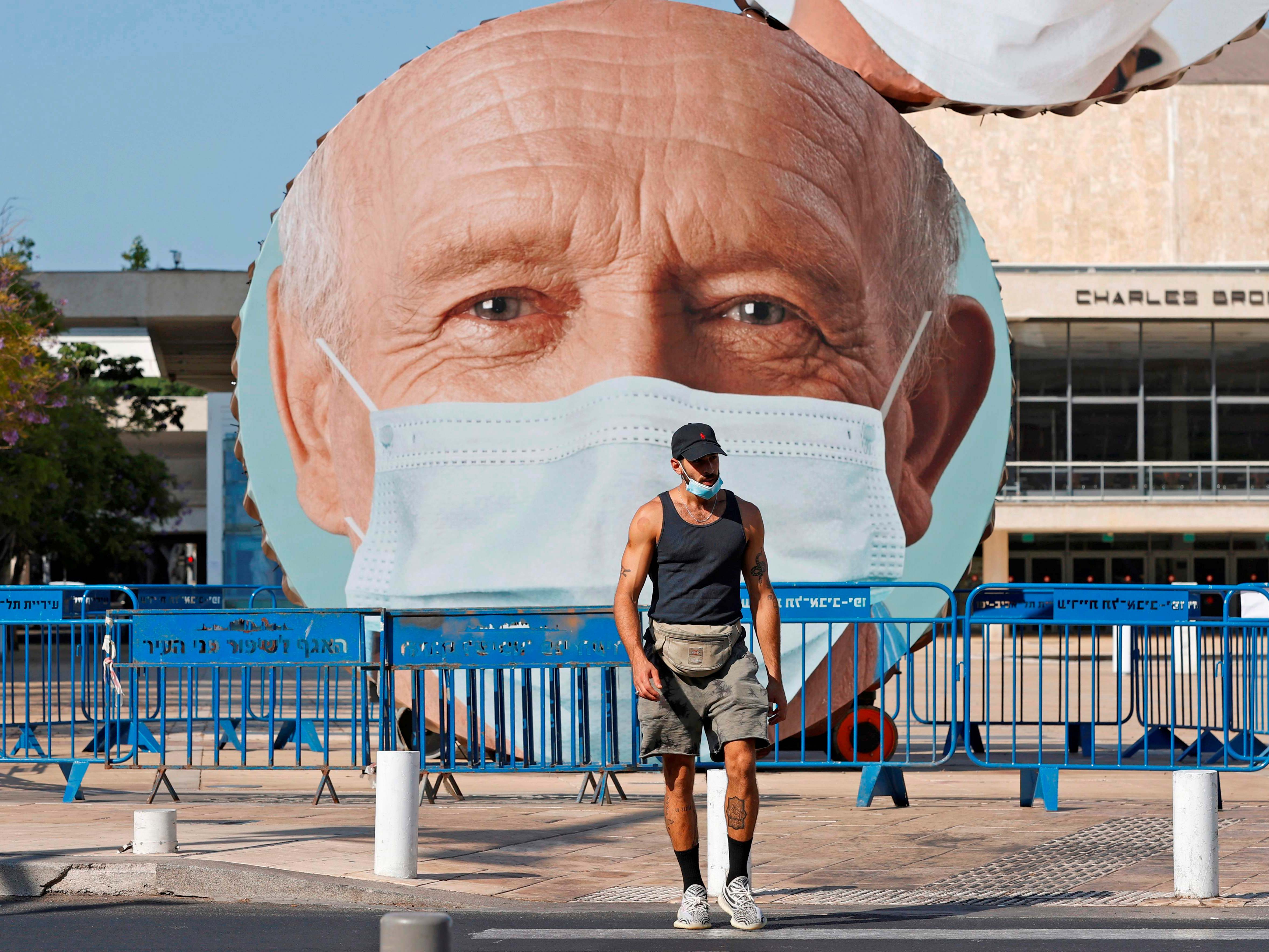 Seorang pejalan kaki berpakaian bertopeng berjalan di depan patung Hitromemut karya seniman Israel Menashe Kadishman.