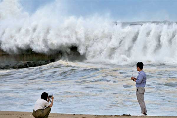 Sepasang suami istri mengambil foto dengan latar ombak tinggi yang terempas melintasi tanggul laut saat topan Haishen menerjang