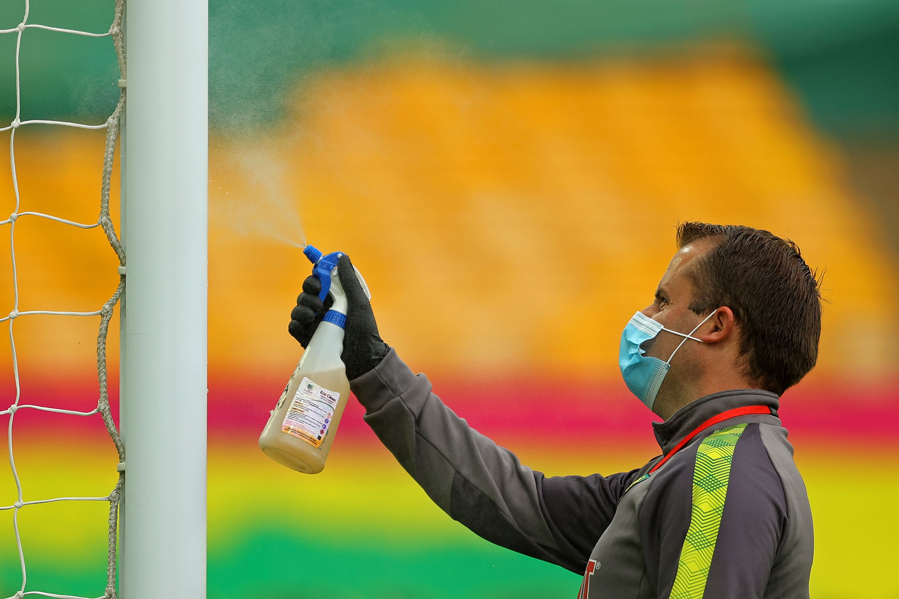 Seorang petugas menyemprotkan cairan disinfektan ke mistar gawang di Carrow Road, Inggris.