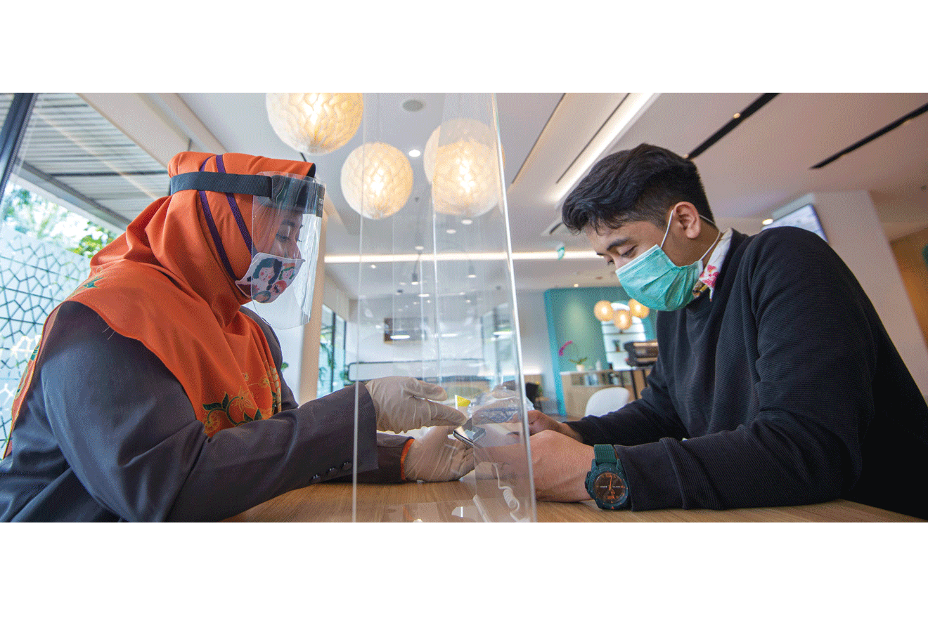 Petugas dengan bermasker, berpelindung wajah, dan bersarung tangan, sedang melayani nasabah salah satu bank syariah, di Jakarta.