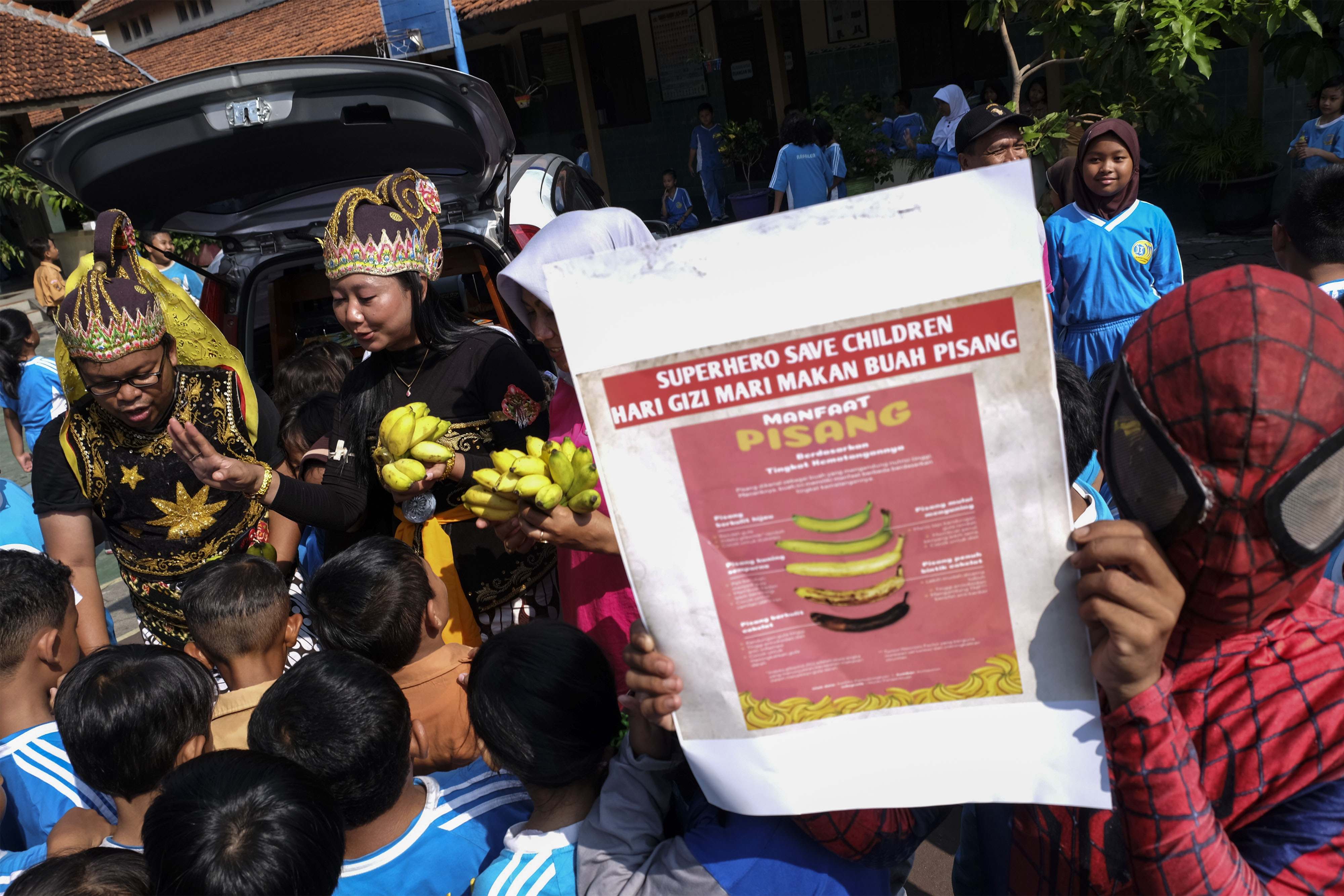 Relawan berkostum wayang dan tokoh animasi membagikan buah pisang kepada siswa SD Negeri Cemara 2 di Solo, Jawa Tengah, Jumat (24/1)