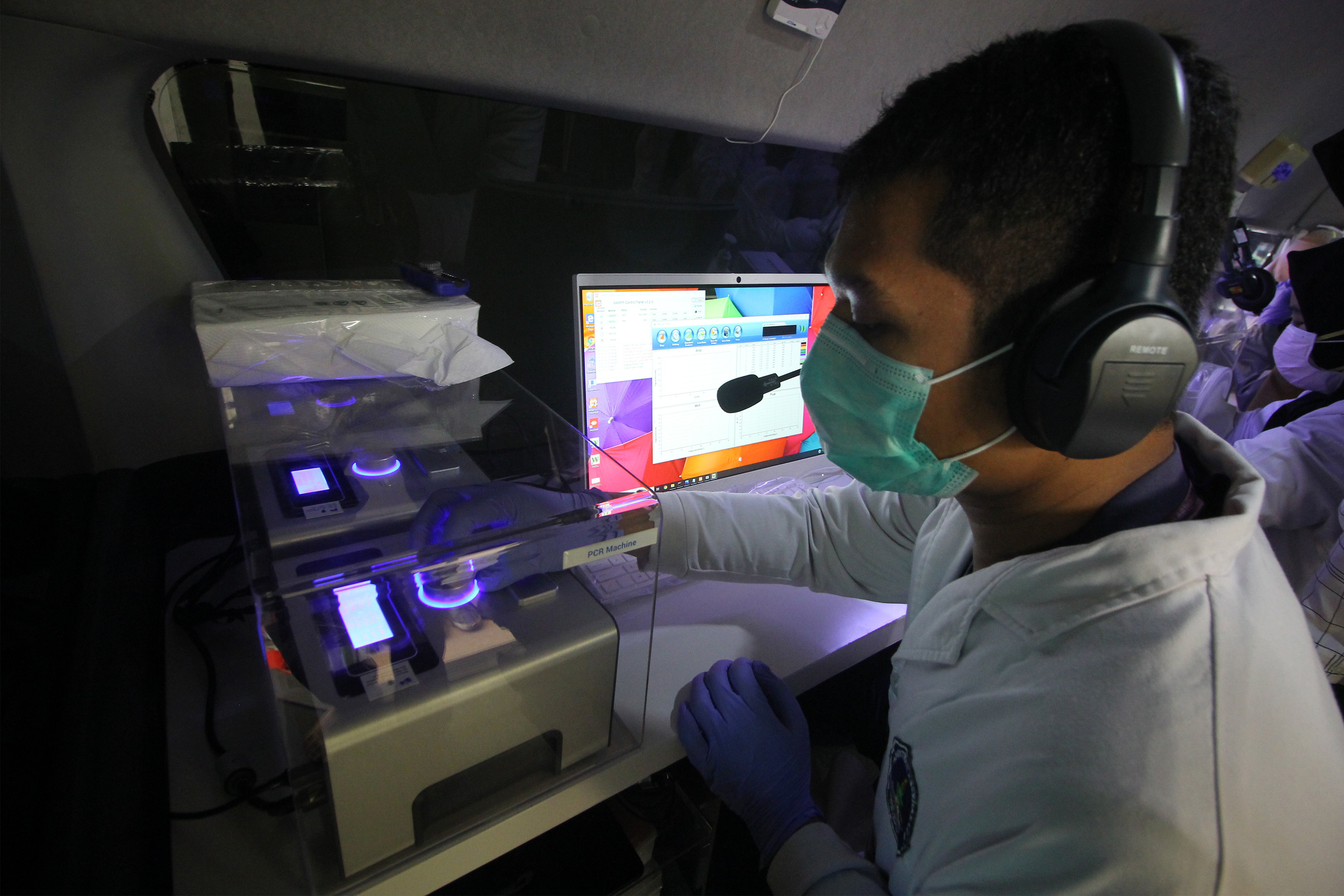  Tenaga kesehatan mengoperasikan mesin Polymerase Chain Reaction (PCR) di dalam mobil lab molekuler.