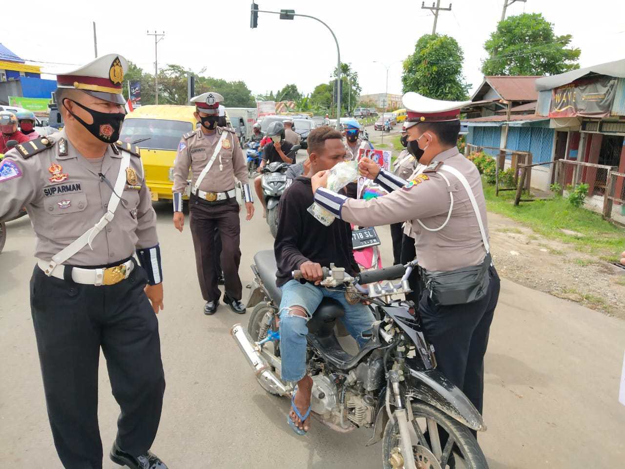Anggota Polres Sorong memasangkan masker pada warga yang melintas.