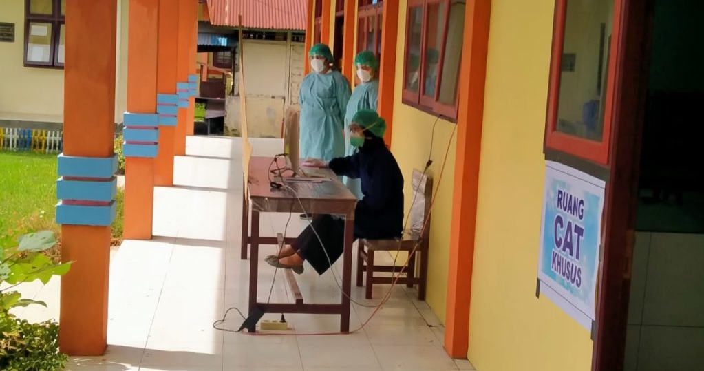 AW. salah satu peserta SKB CPNS yang positif covid-19, saat mengikuti seleksi di teras lokasi tes dikawal petugas yang mengenakan APD.