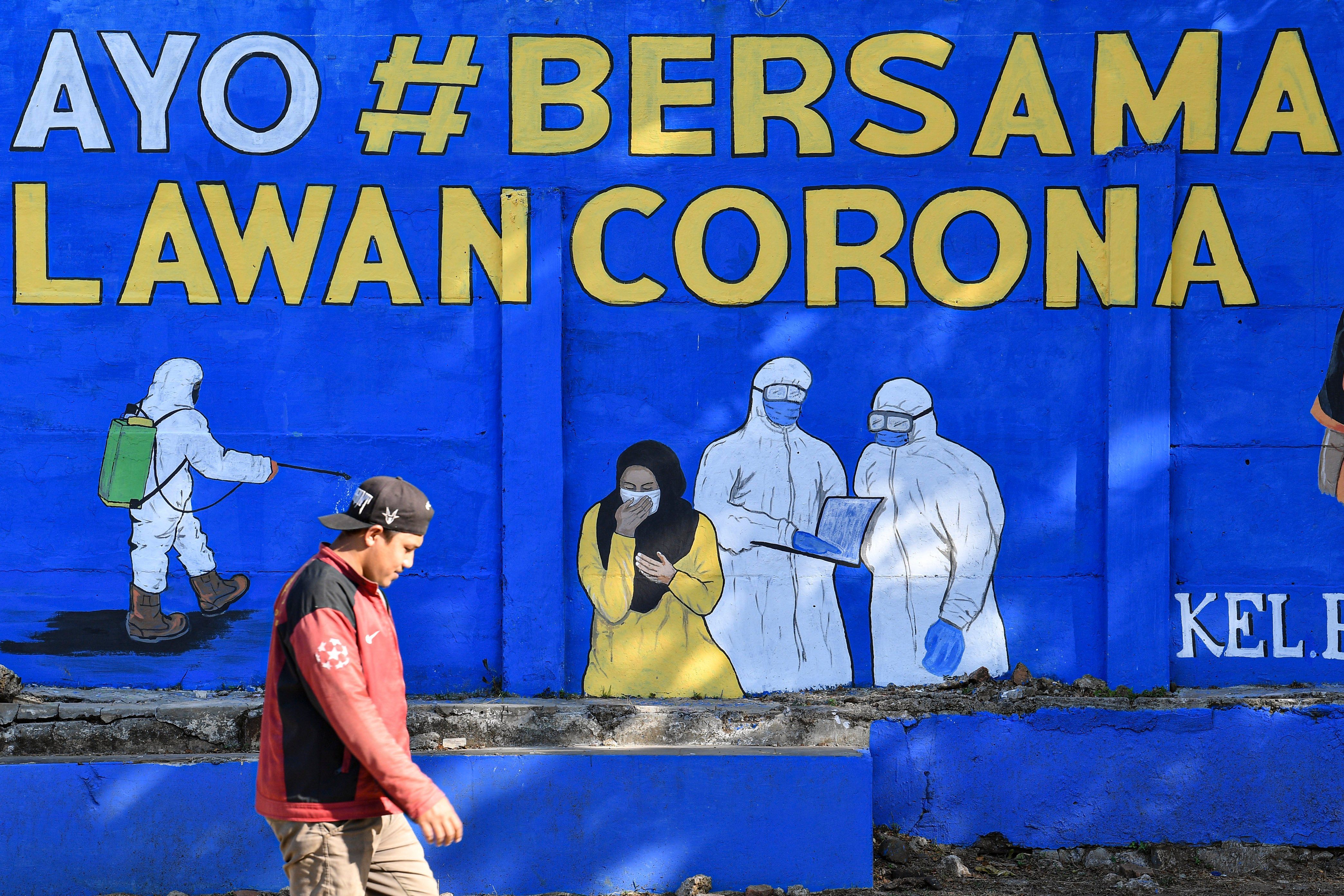 Seorang warga tidak mengenakan masker saat melintasi mural terkait covid-19 di Tebet, Jakarta.