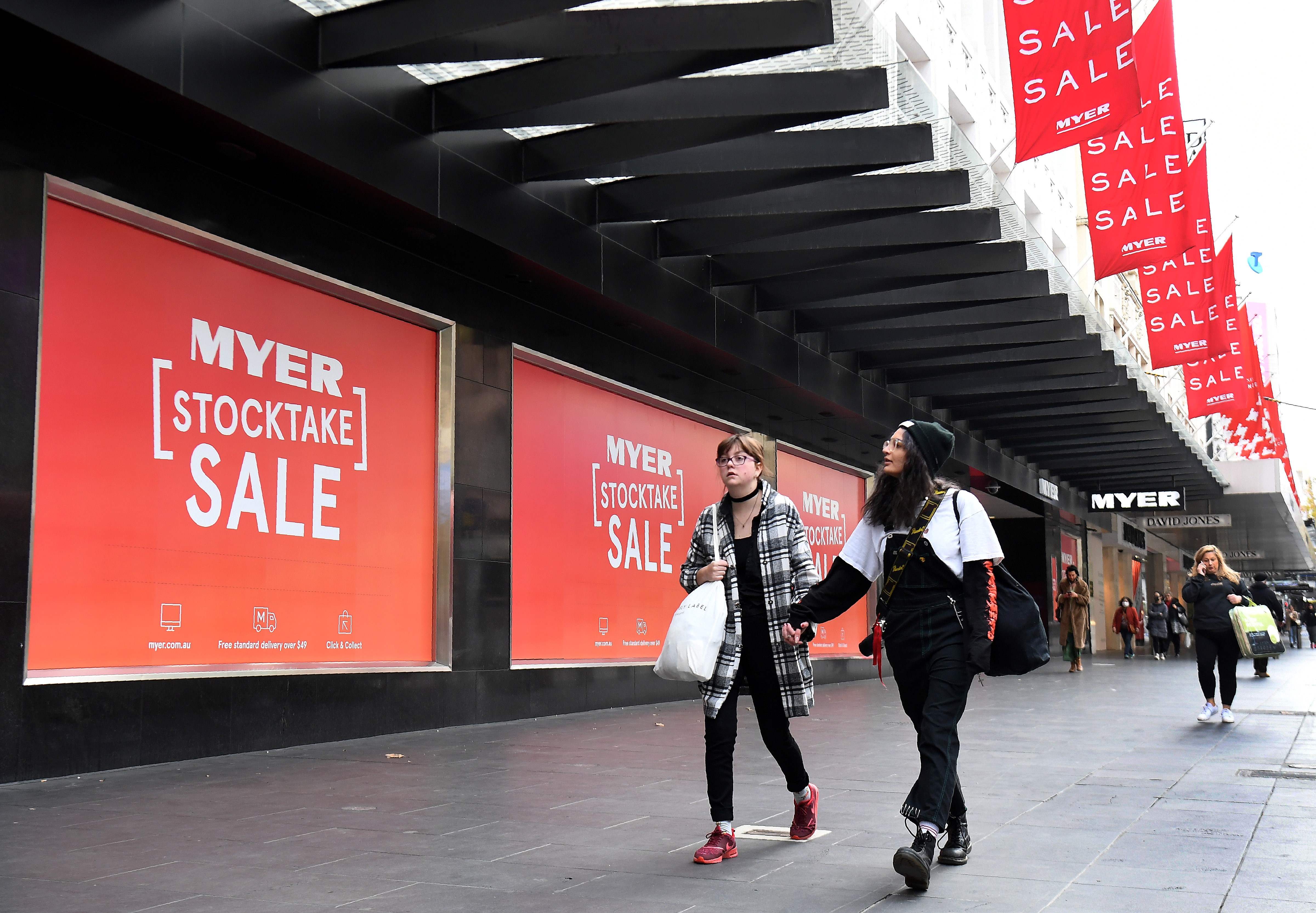 Dua warga melewati poster sale di sebuah pusat perbelanjaan di Melbourne, Australia.