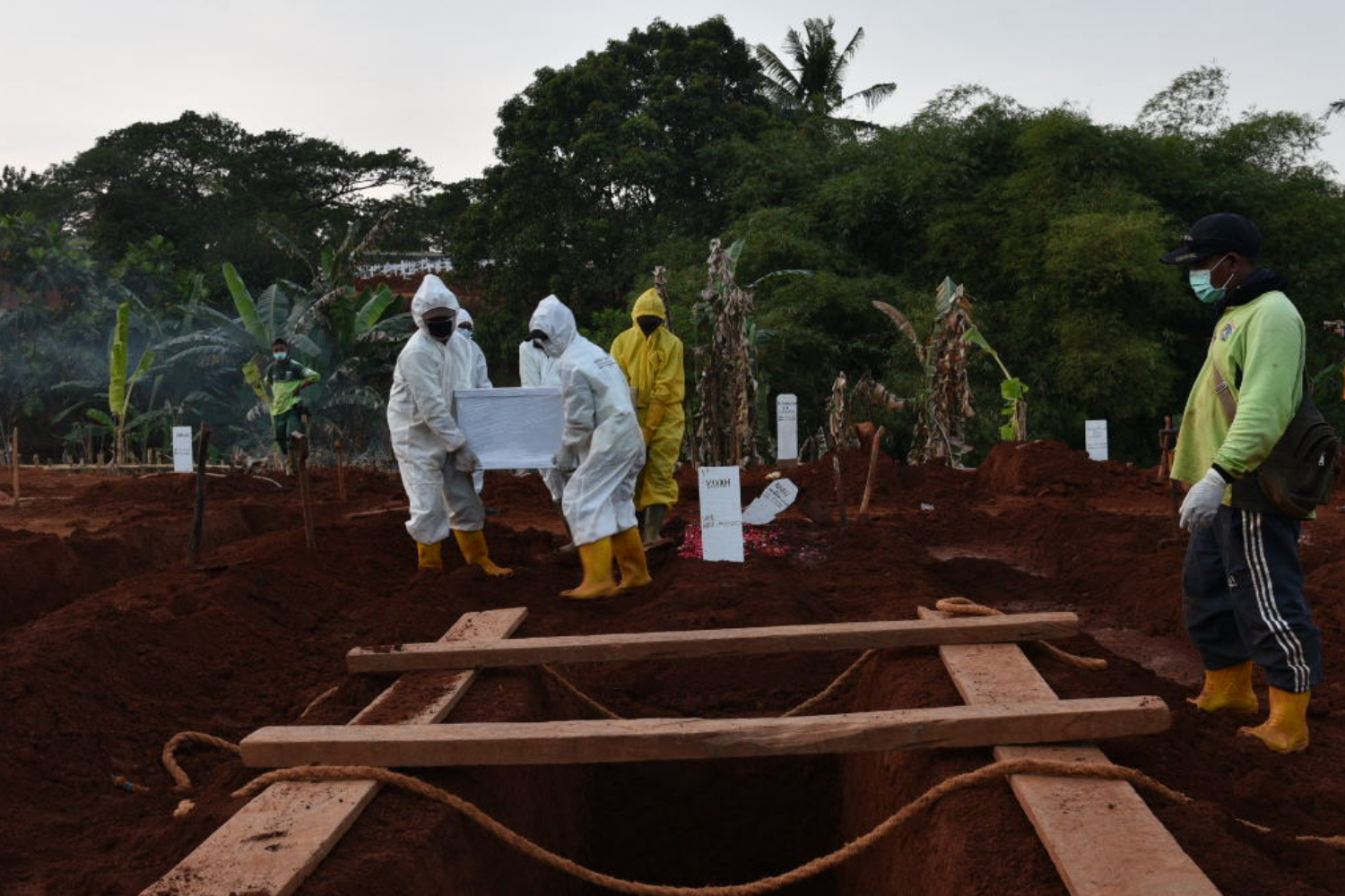 Petugas pemakaman penanganan jenazah pasien covid-19 menurunkan peti jenazah ke dalam pusara di TPU Pondok Ranggon, Jakarta Timur
