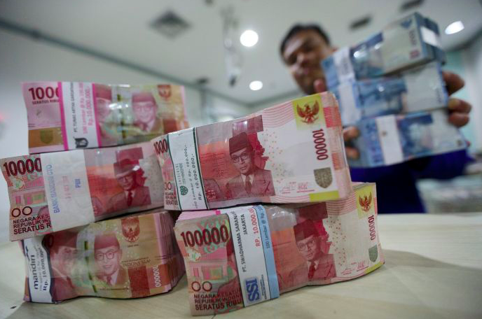 Karyawan bank menghitung tumpukan uang rupiah. 