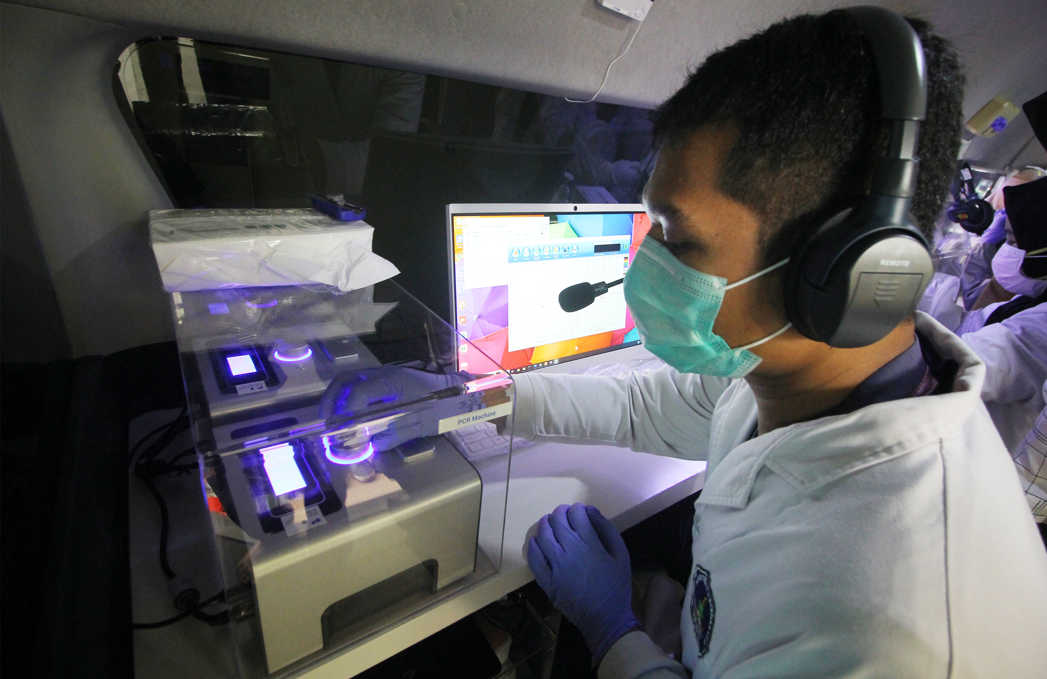 Tenaga kesehatan mengoperasikan mesin Polymerase Chain Reaction (PCR) di dalam mobil lab molekuler