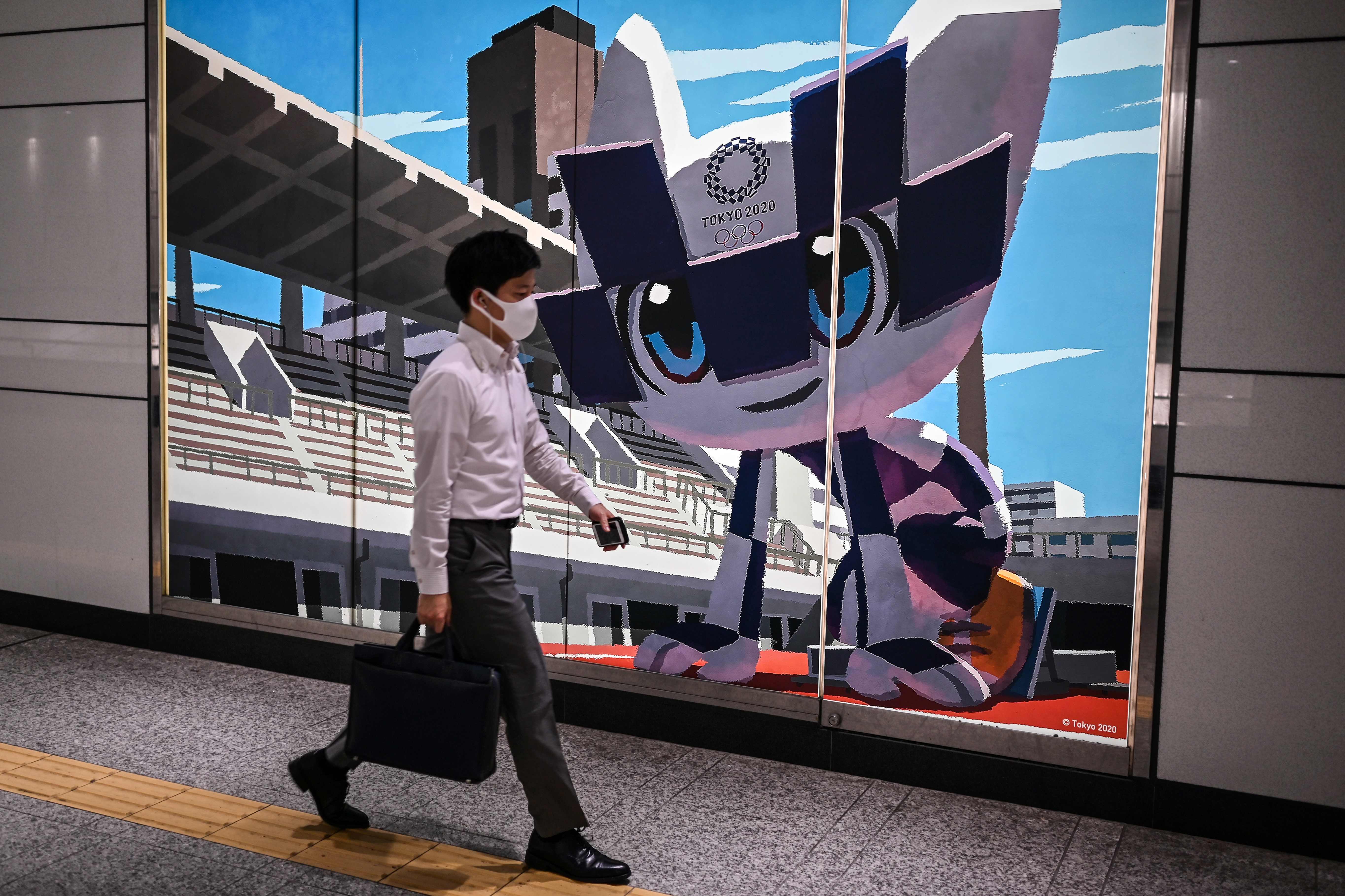Seorang warga berjalan di depan gambar maskot Olimpiade Tokyo.