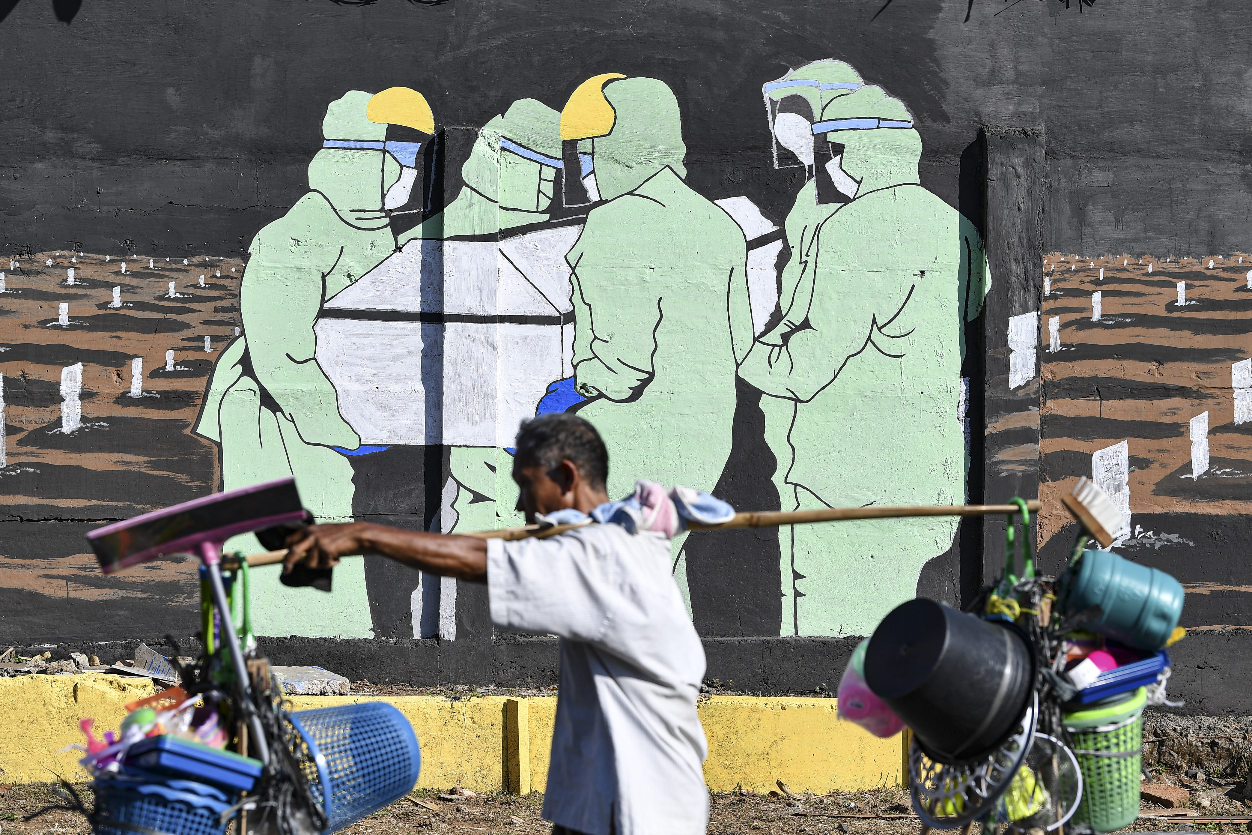 Pedagang yang tidak mengenakan masker melintasi mural terkait covid-19 di kawasan Tebet, Jakarta.