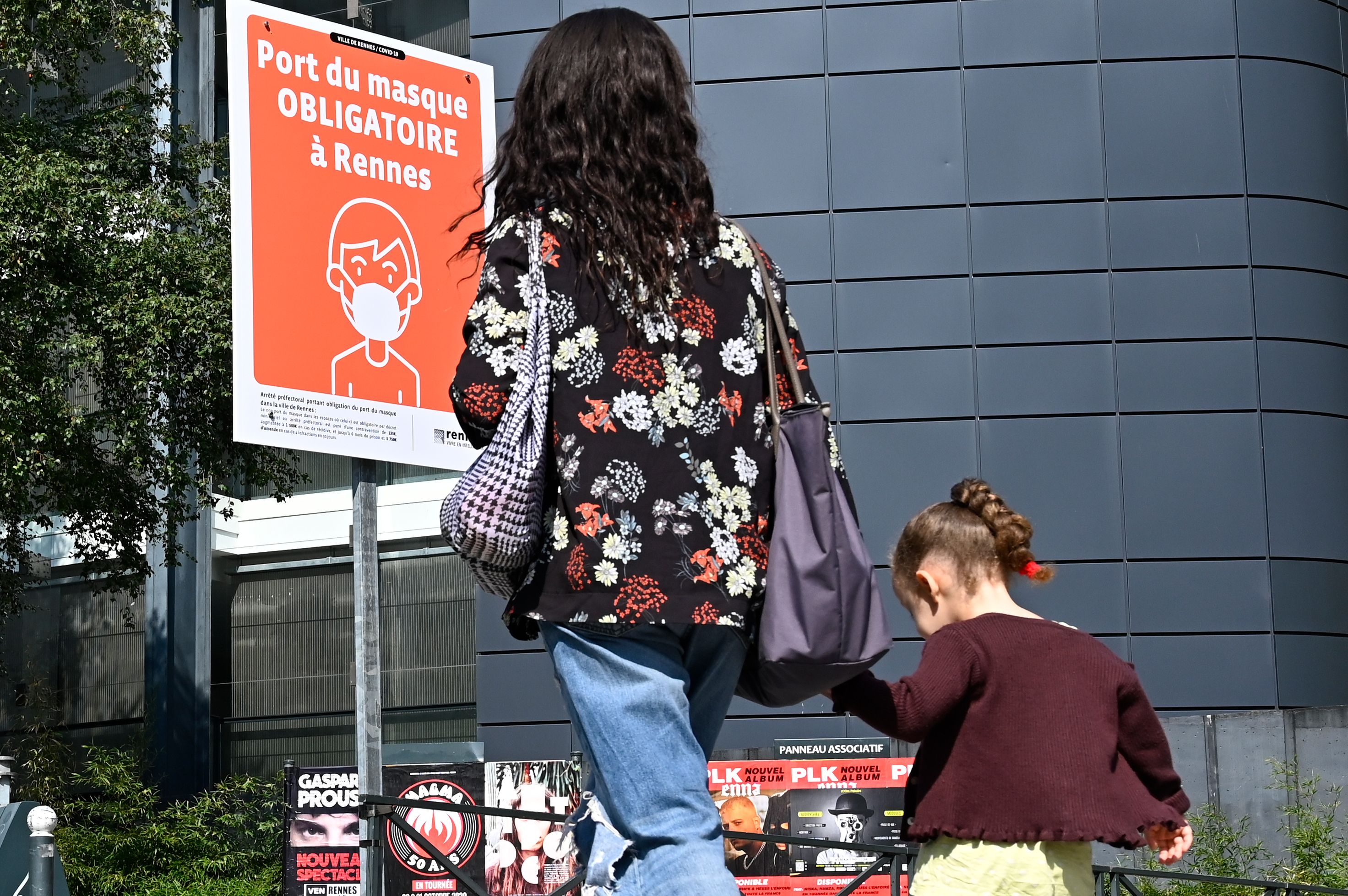 Warga melintas di depan papan pengumuman yang berbunyi 'Penggunaan masker wajib di Rennes' di Kota Rennes, Prancis.