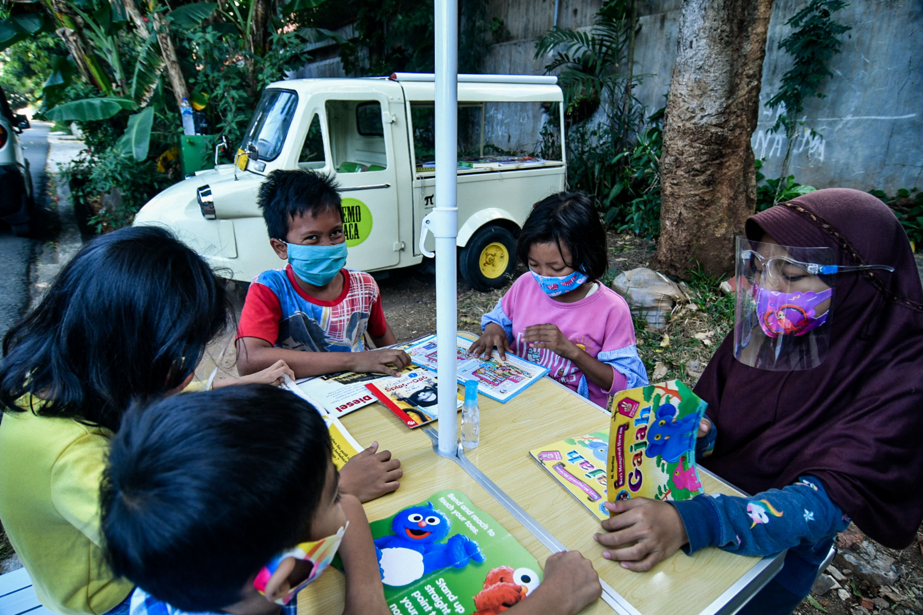 Anak-anak membaca buku koleksi dari Bemo Baca milik Sutino, 60, bertepatan dengan Hari Aksara Internasional di Jakarta, kemarin.