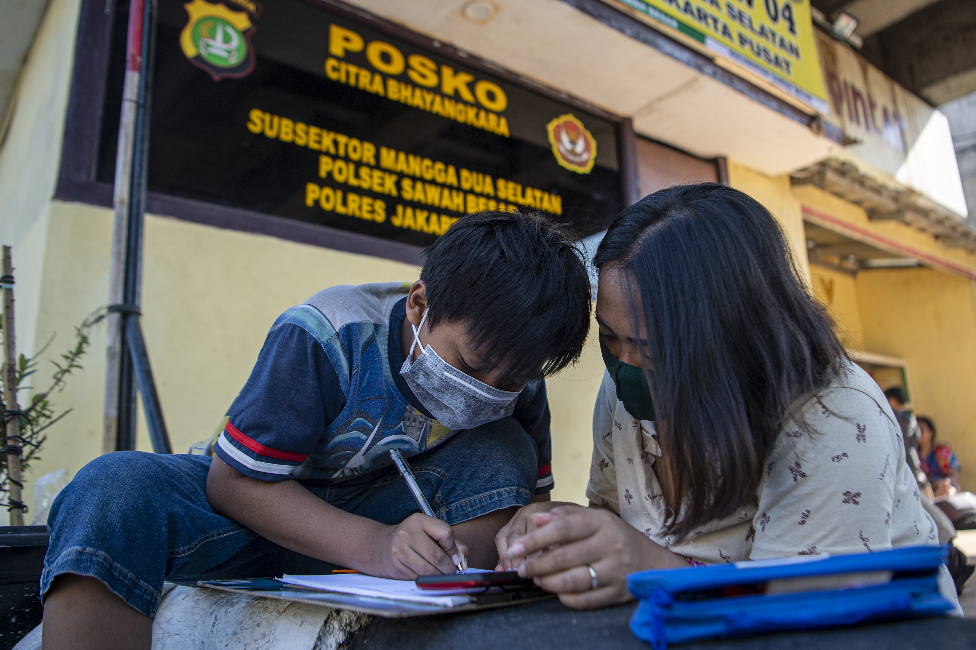 Orangtua siswa membimbing anaknya belajar daring memanfaatkan jaringan internet gratis di kolong rel kereta api Mangga Besar, Jakarta.